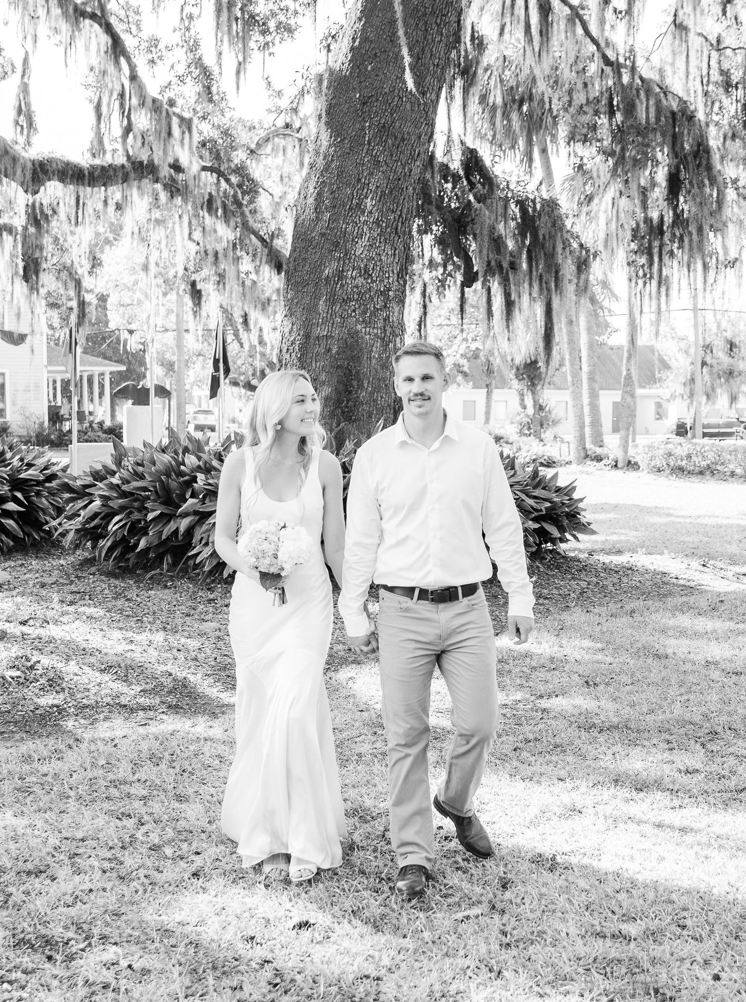 Black and white photo of a wedding couple walking under Spanish moss covered trees.