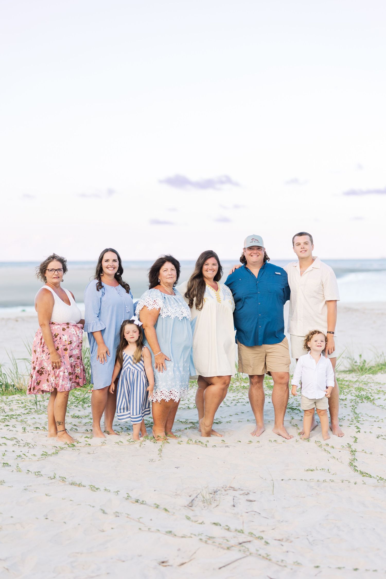 Extended family group enjoying time together on a sandy beach during golden hour in casual summer attire.