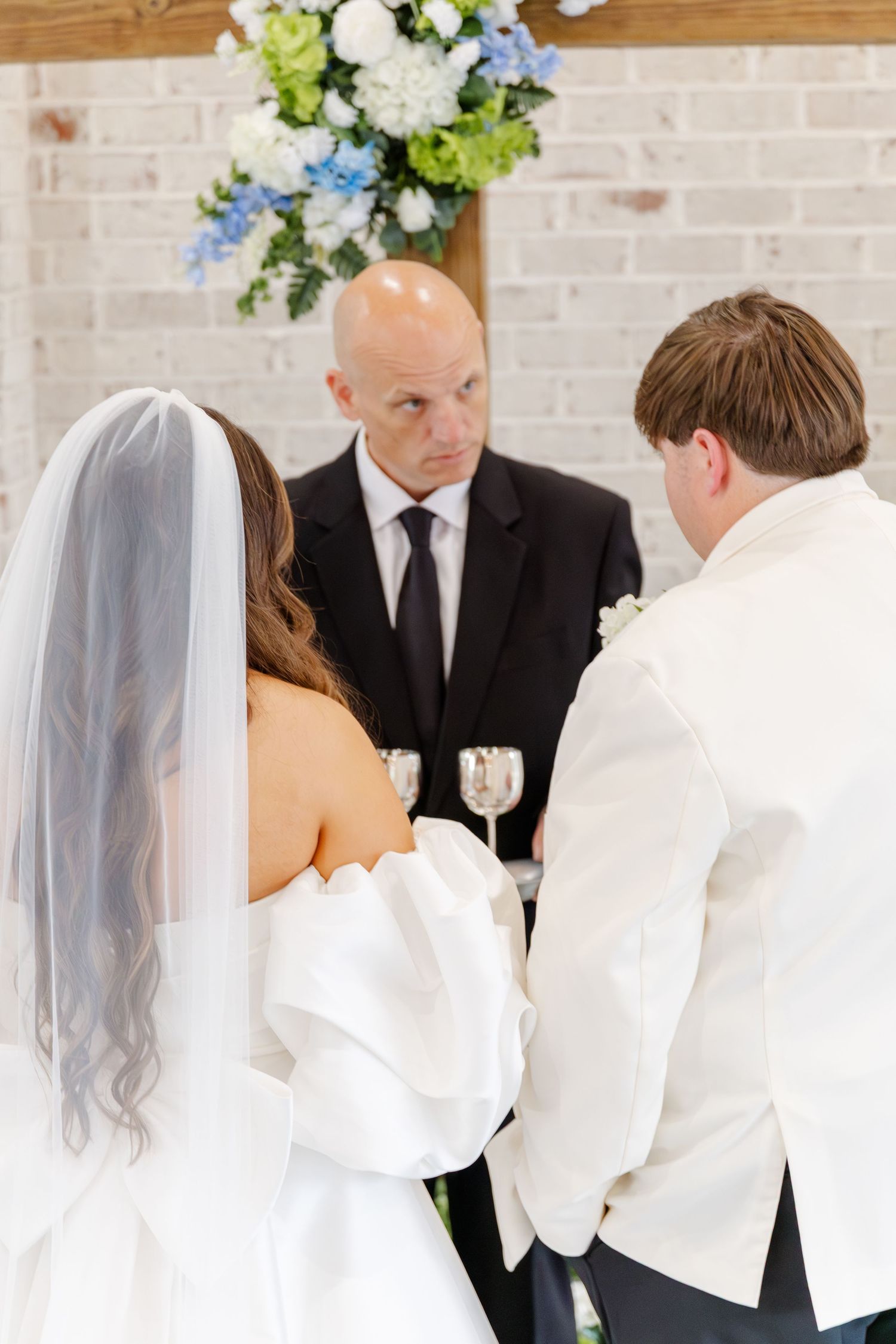 Bride and groom exchanging vows before officiant at altar decorated with blue and white florals.