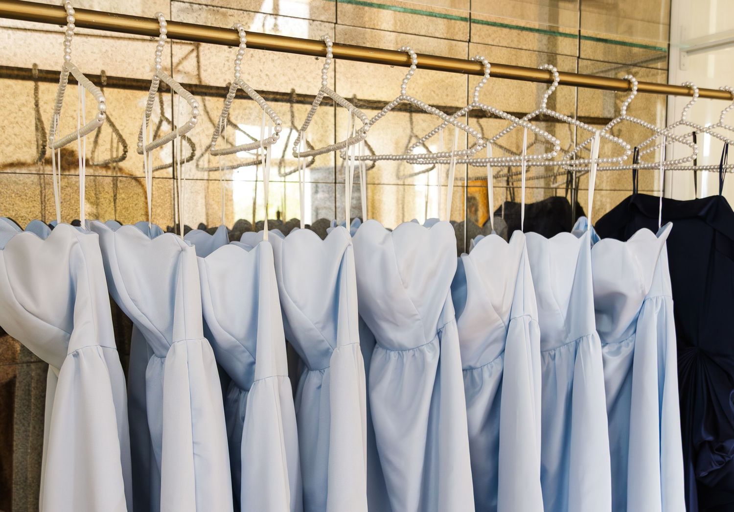 Light blue bridesmaid dresses hanging on silver hangers in a row on a clothing rack.