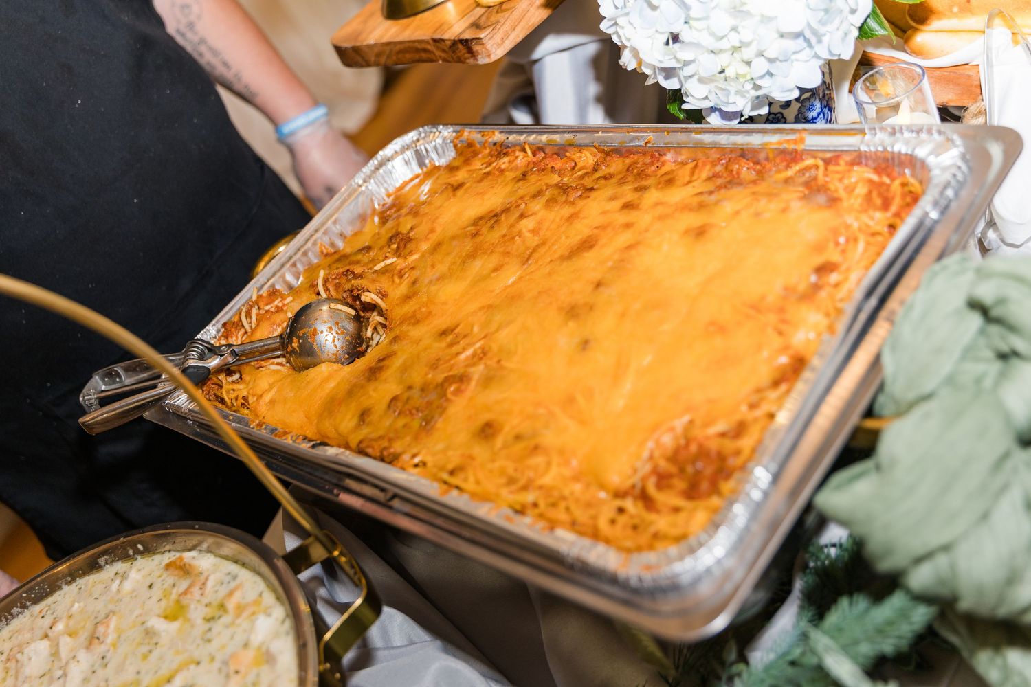 Golden-baked cheesy lasagna served in a large aluminum catering pan at a wedding reception buffet.