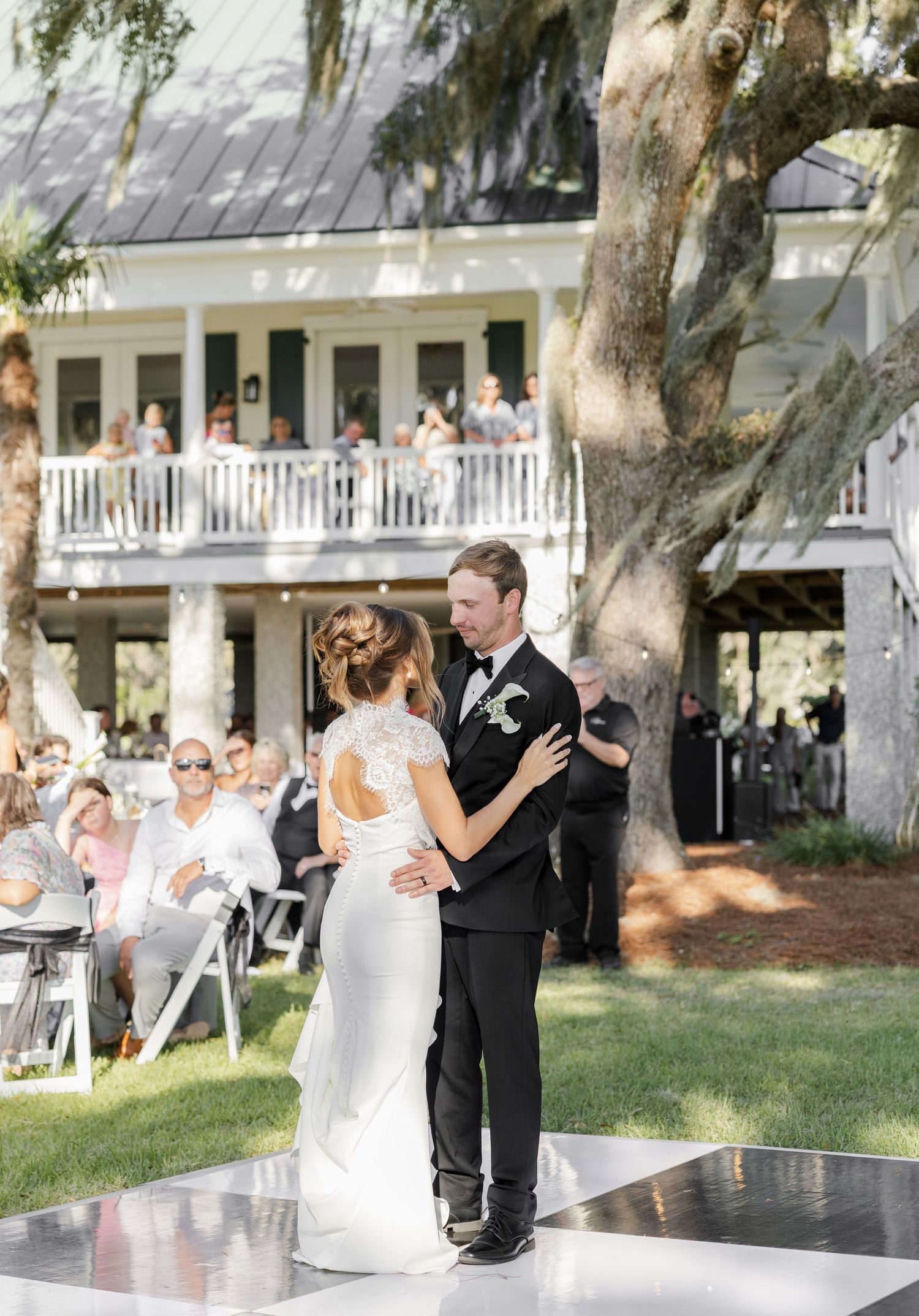 Bride and groom share their first dance on outdoor dance floor at elegant Southern wedding venue with Spanish moss trees.