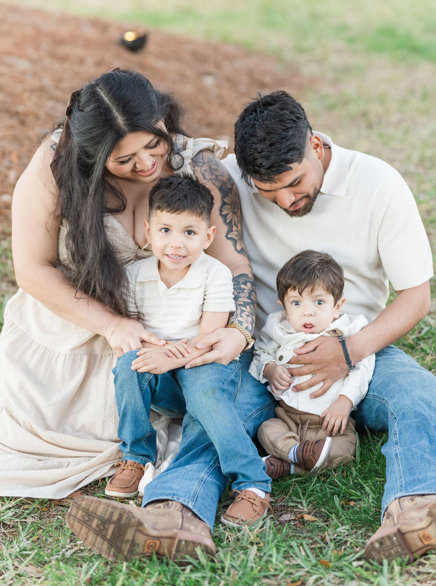Family sitting together on grass enjoying tender moments in a park setting.