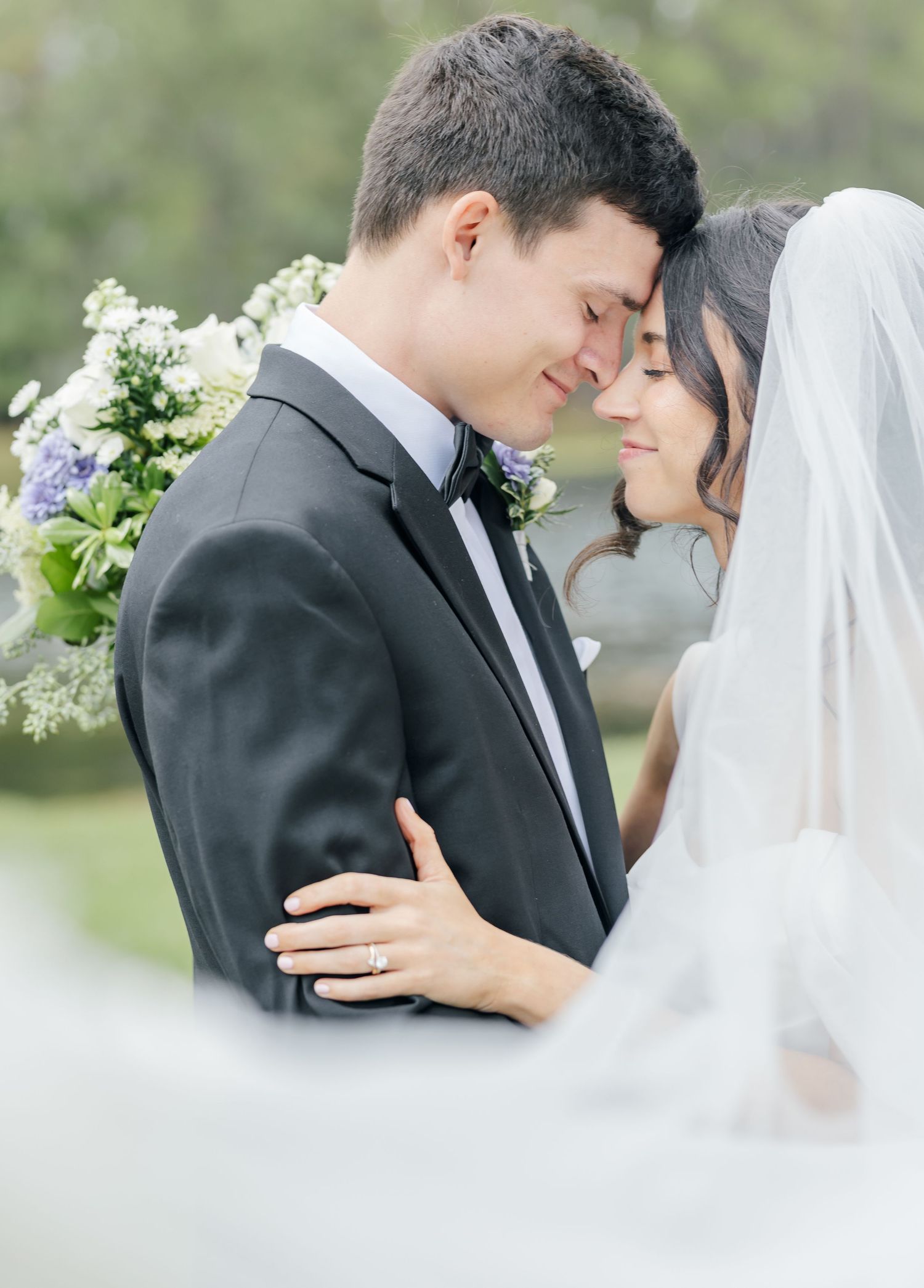 Romantic outdoor wedding moment captured in soft focus with white floral arrangements in the background.
