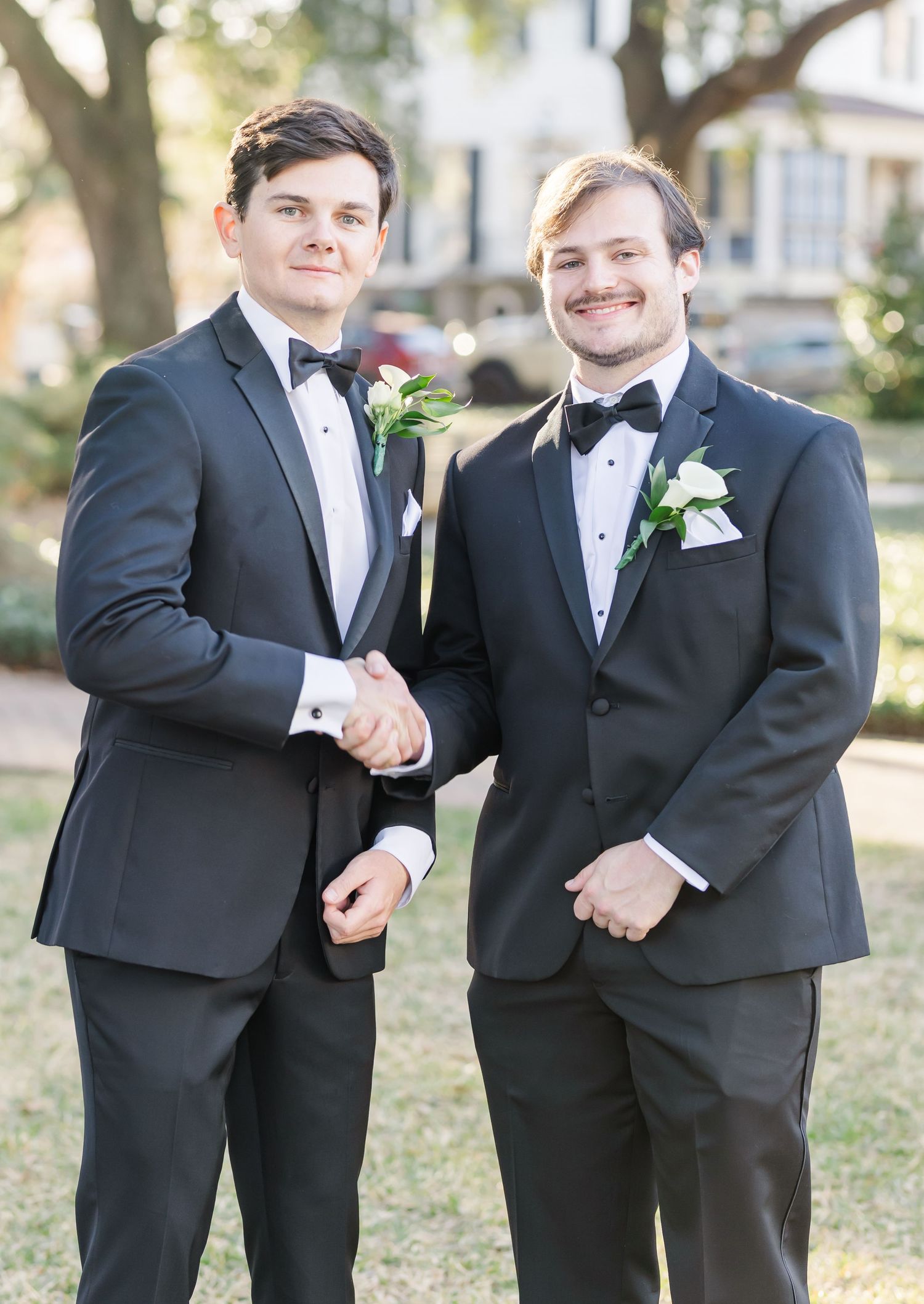 Groomsmen in black tuxedos share candid moments and laughter during outdoor wedding photo session.