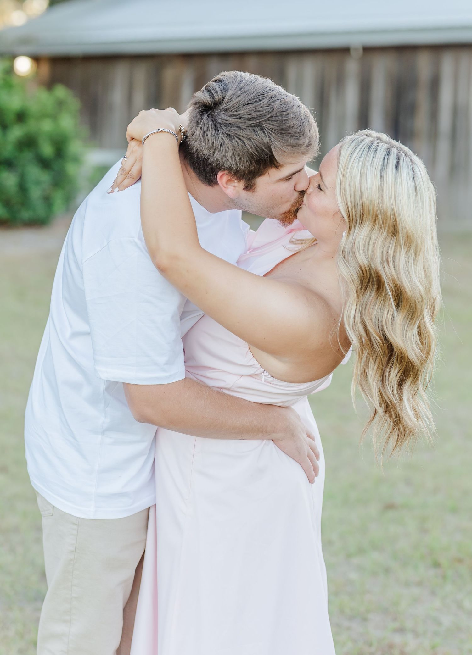 Couple sharing intimate moments in casual white outfits against a natural outdoor backdrop.