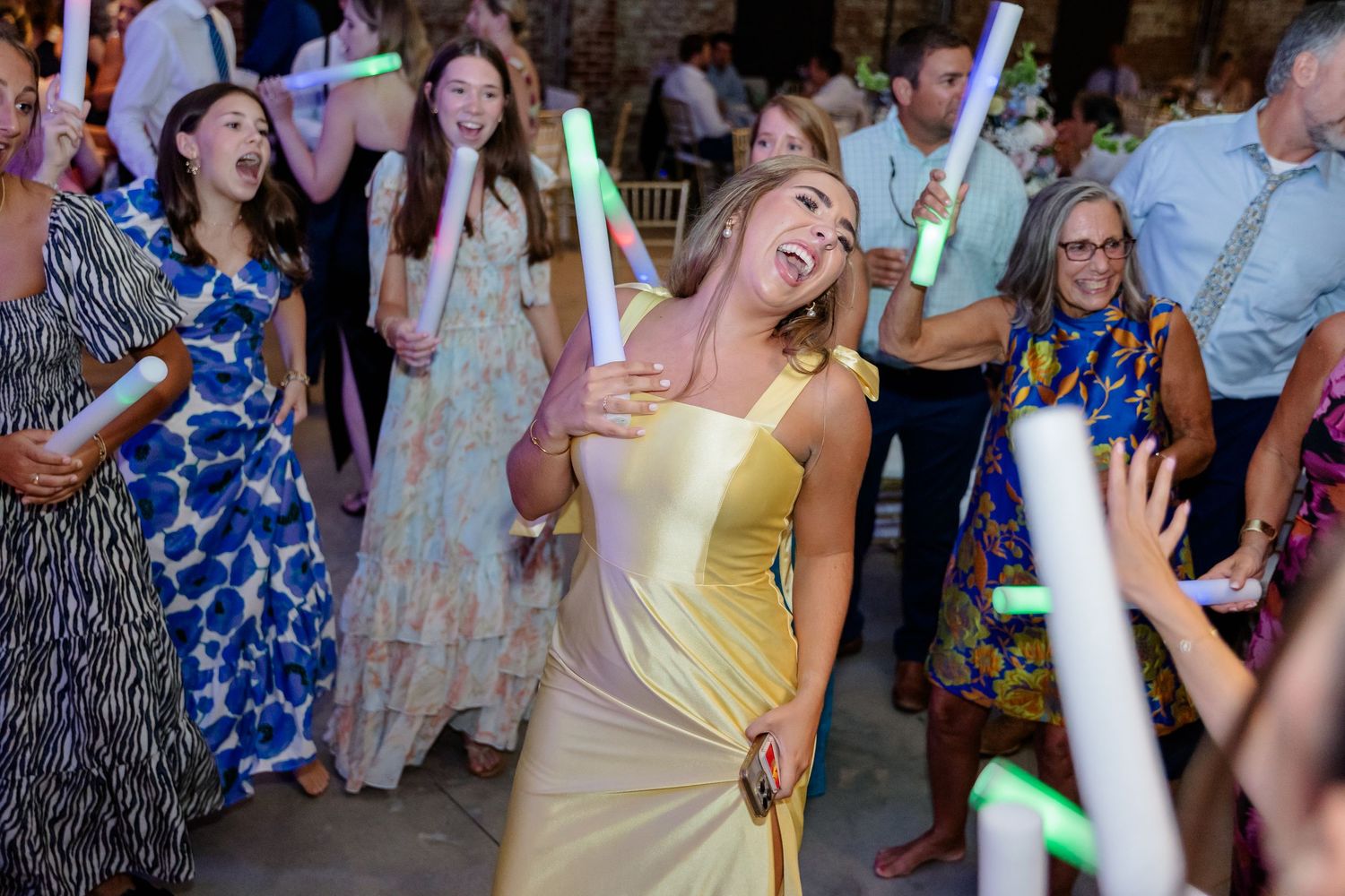 Guests enjoying a dance party with colorful light sticks at a wedding celebration.