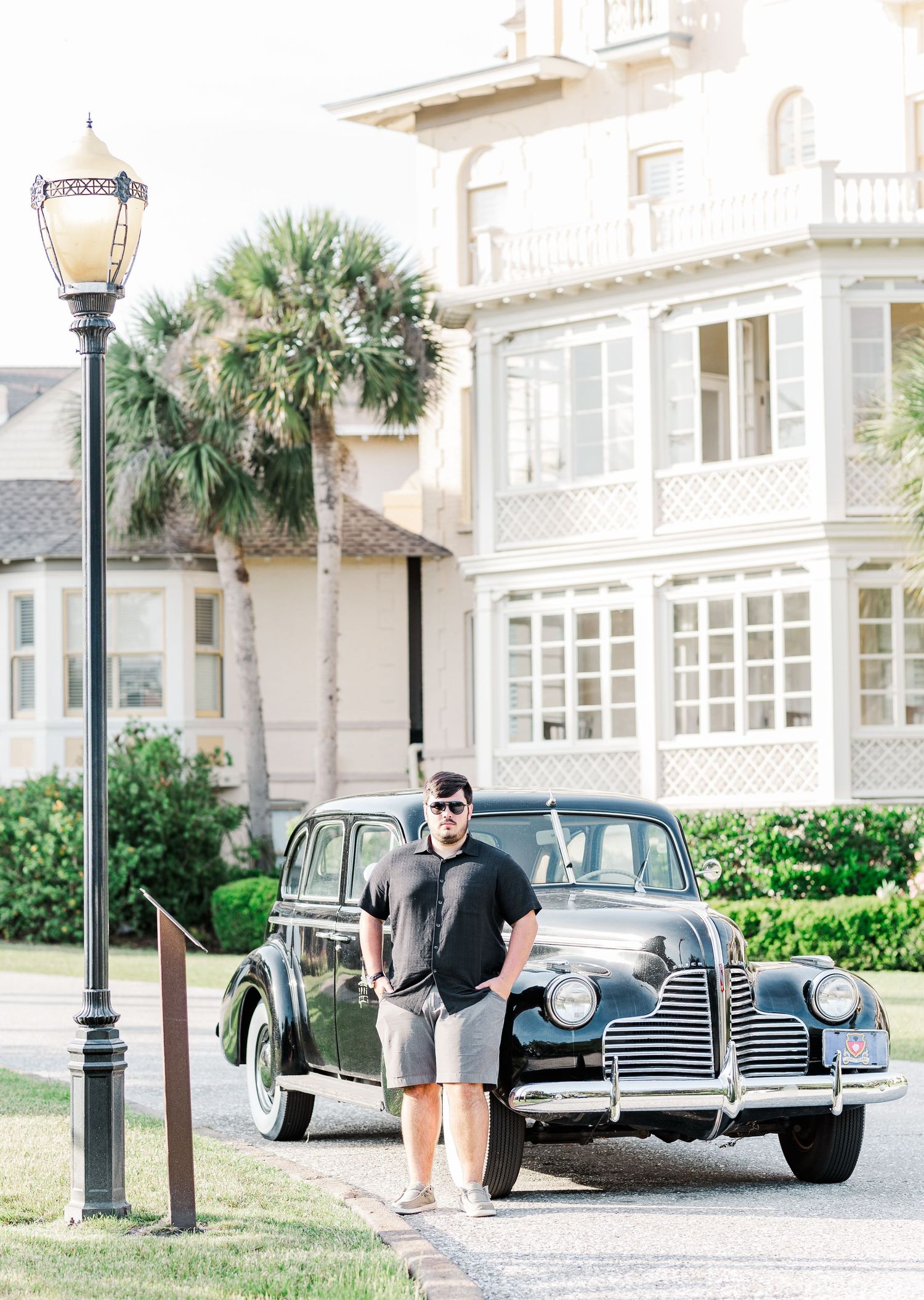 Classic vintage automobiles parked along a palm-lined street with historic architecture in the background.