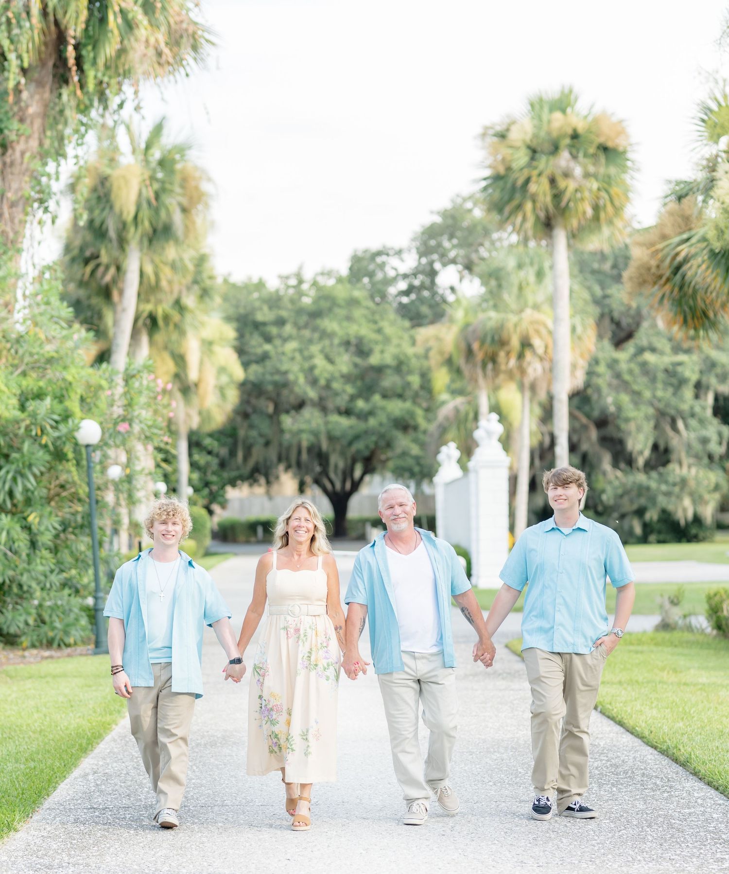 A group walking together on a palm-lined path wearing coordinated light blue and white outfits.