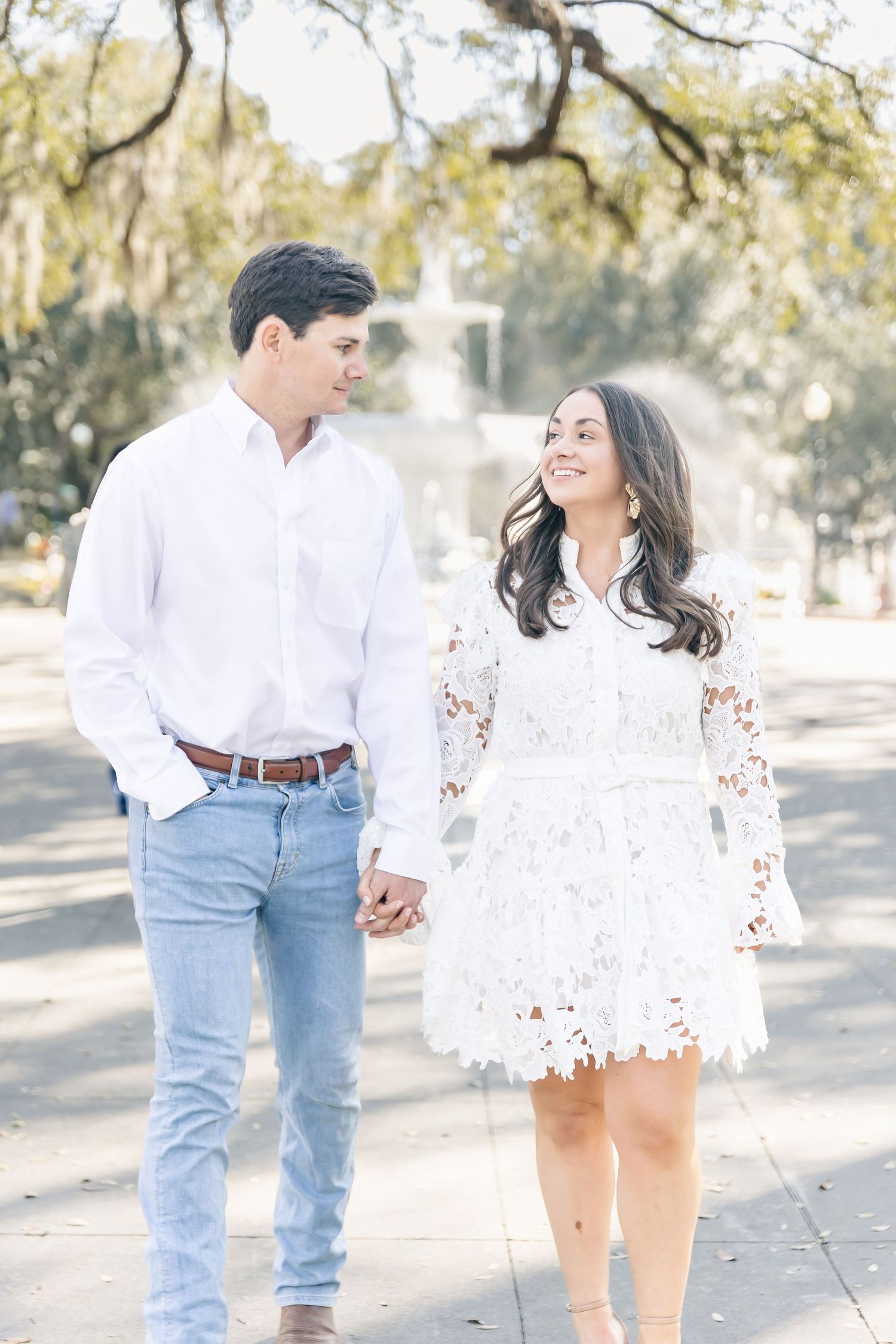 Romantic couple in white and denim casually posing together in a sun-dappled outdoor setting with moss-draped trees.