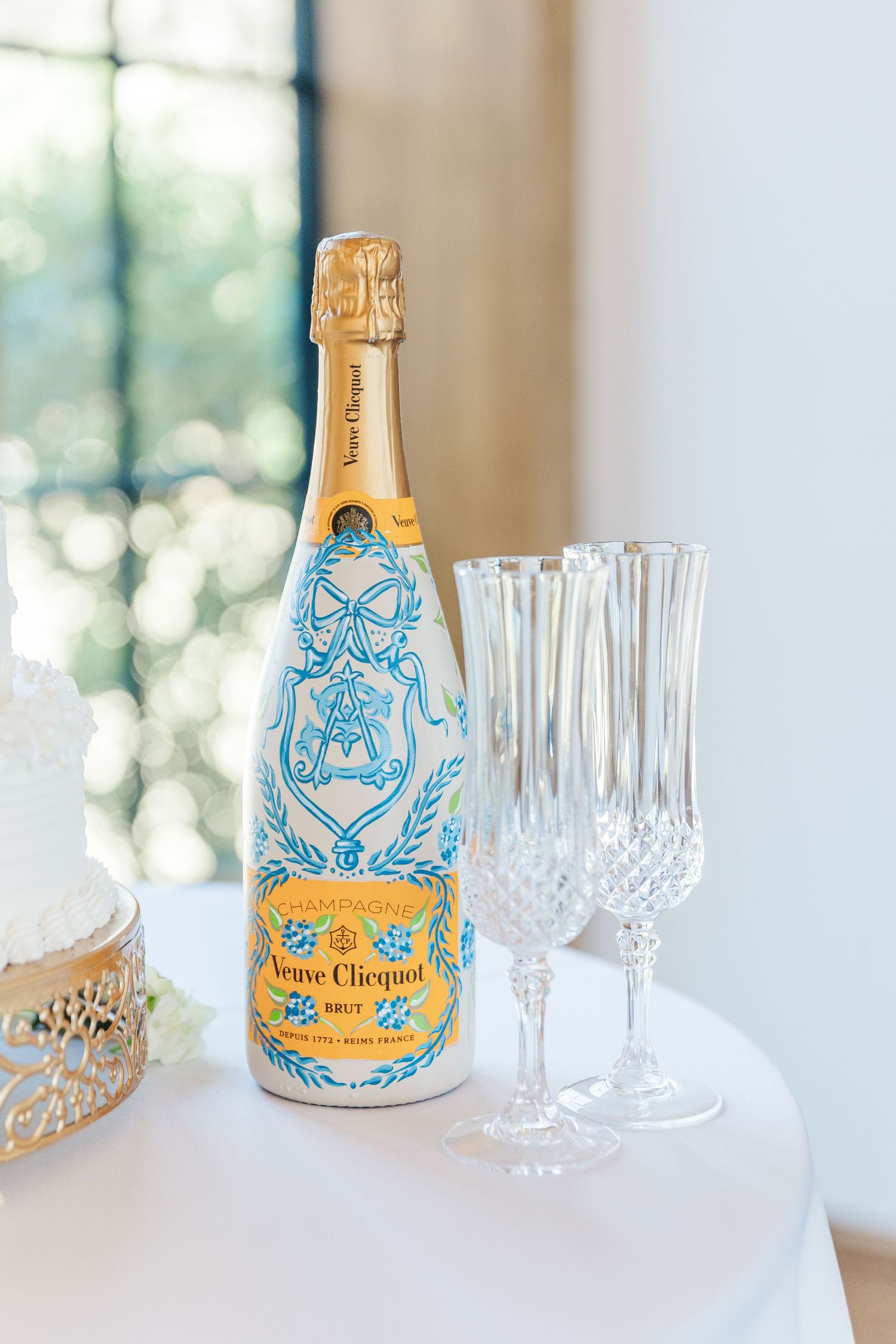 A limited edition Veuve Clicquot champagne bottle with blue and gold decorative design sits beside crystal champagne flutes.
