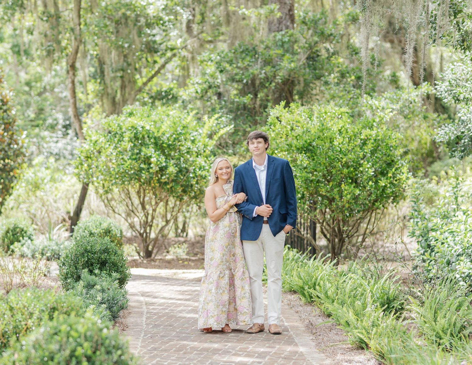 Couple enjoying a romantic stroll along a scenic tree-lined path in a lush garden setting.
