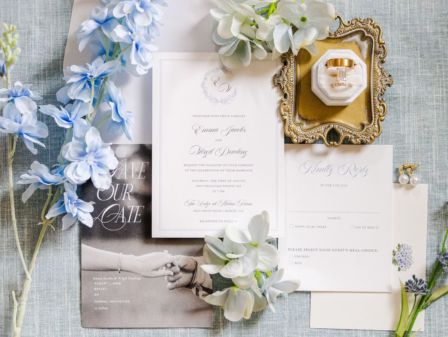 Elegant wedding invitation suite with blue hydrangeas, gold rings, and floral stationery on a soft gray background.