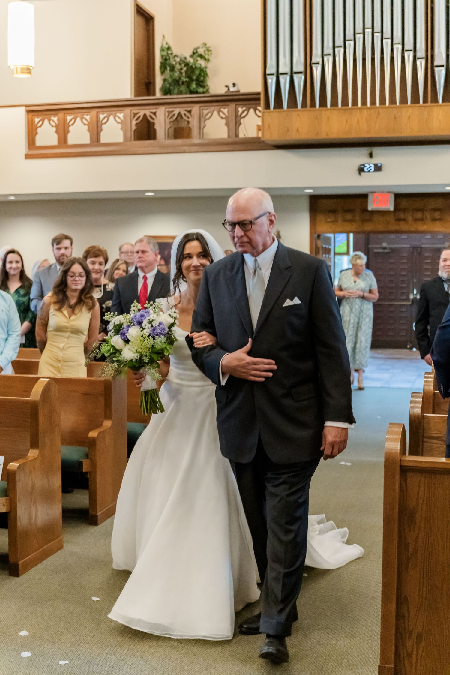 Wedding processional in a church with an organ and wooden pews.