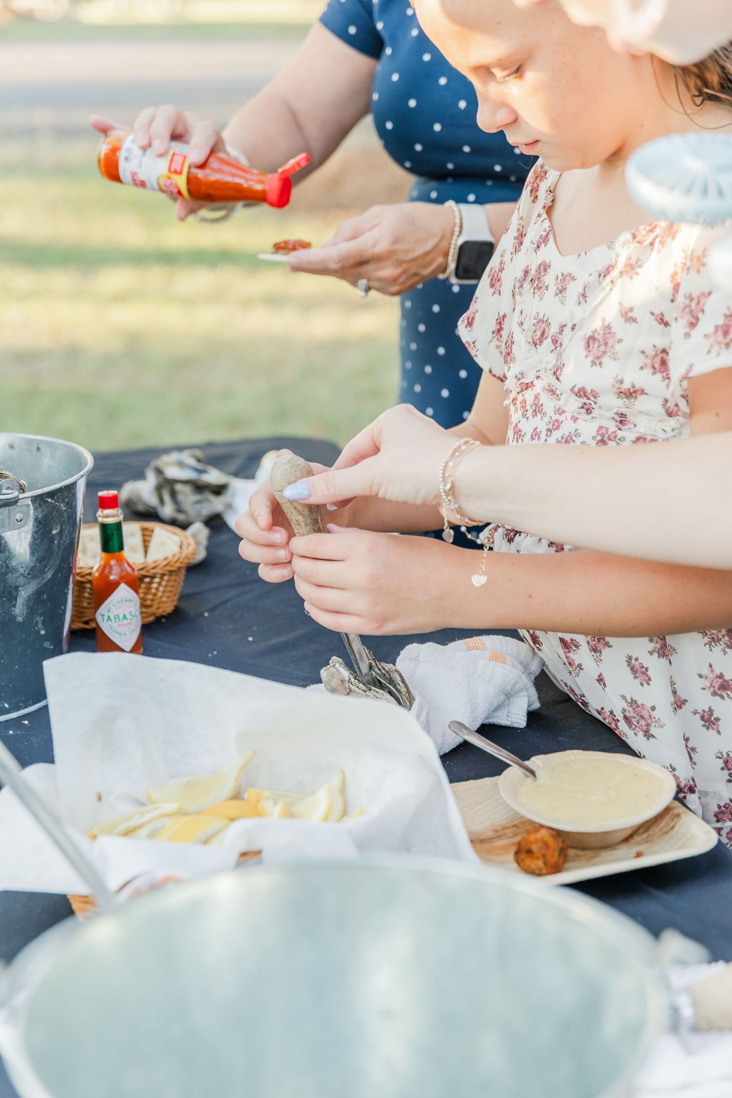 Hands preparing food and ingredients on a dark table surface with plates and utensils.