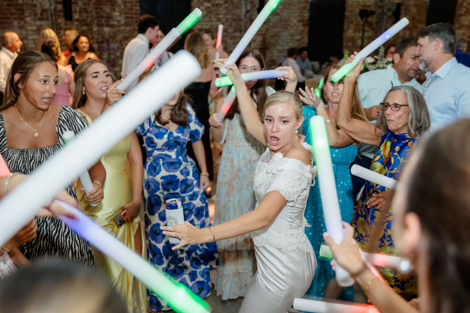Wedding party guests dance and celebrate while holding glowing green light sticks on the dance floor.