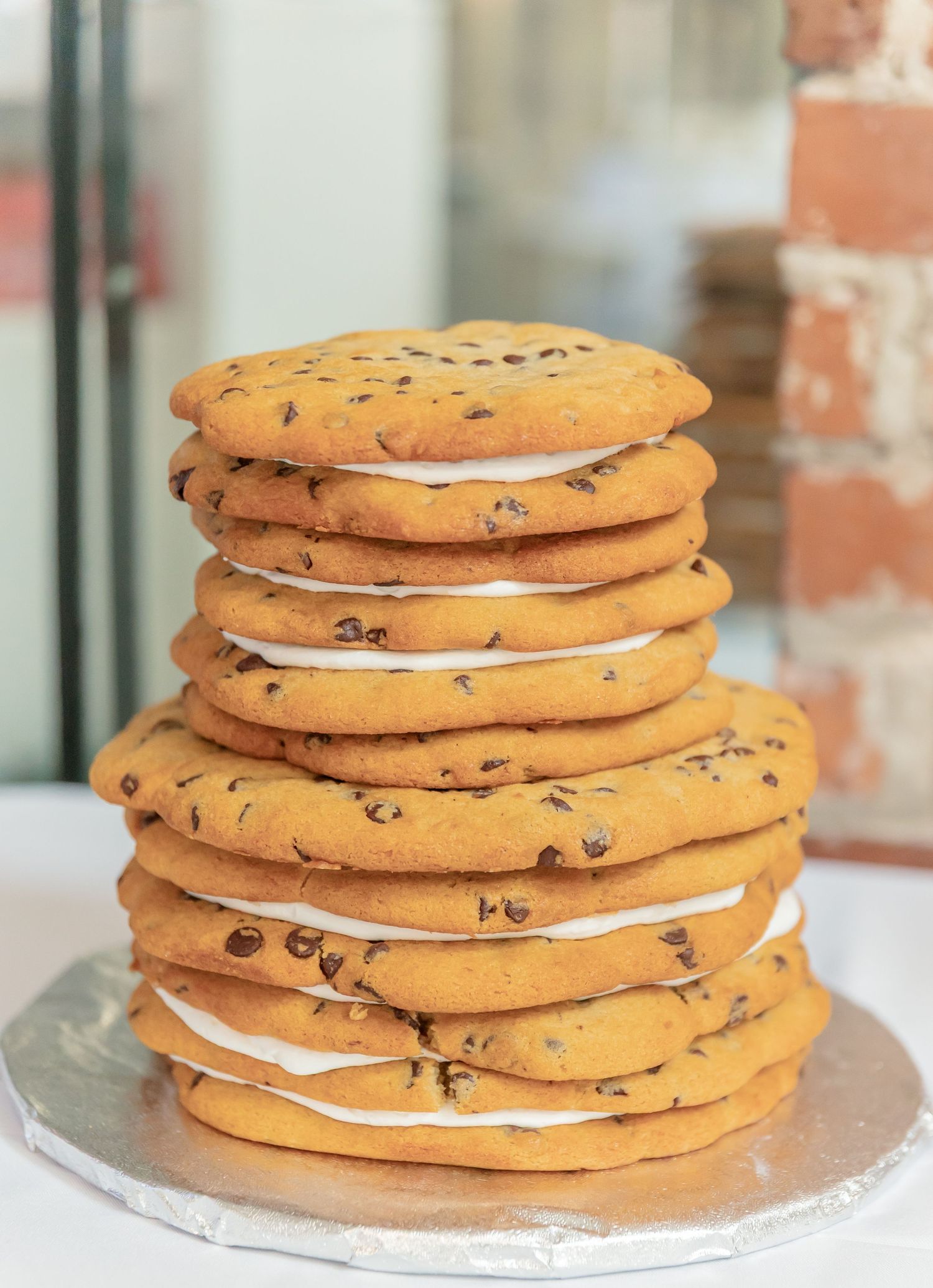 Giant chocolate chip cookie cake stacked in layers with cream filling on a silver platter.
