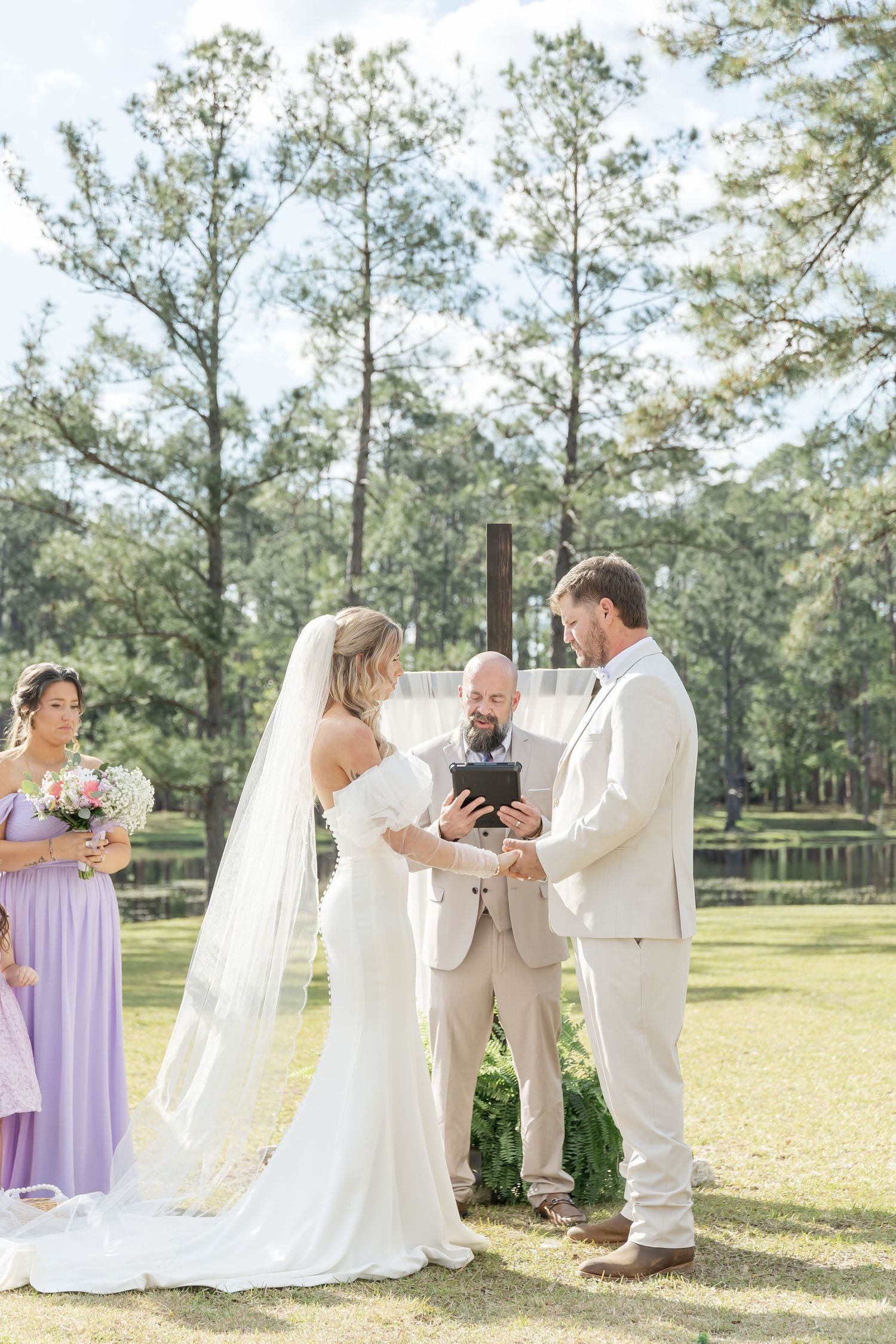 Wedding ceremony in progress with officiant and couple surrounded by pine trees and lake view.