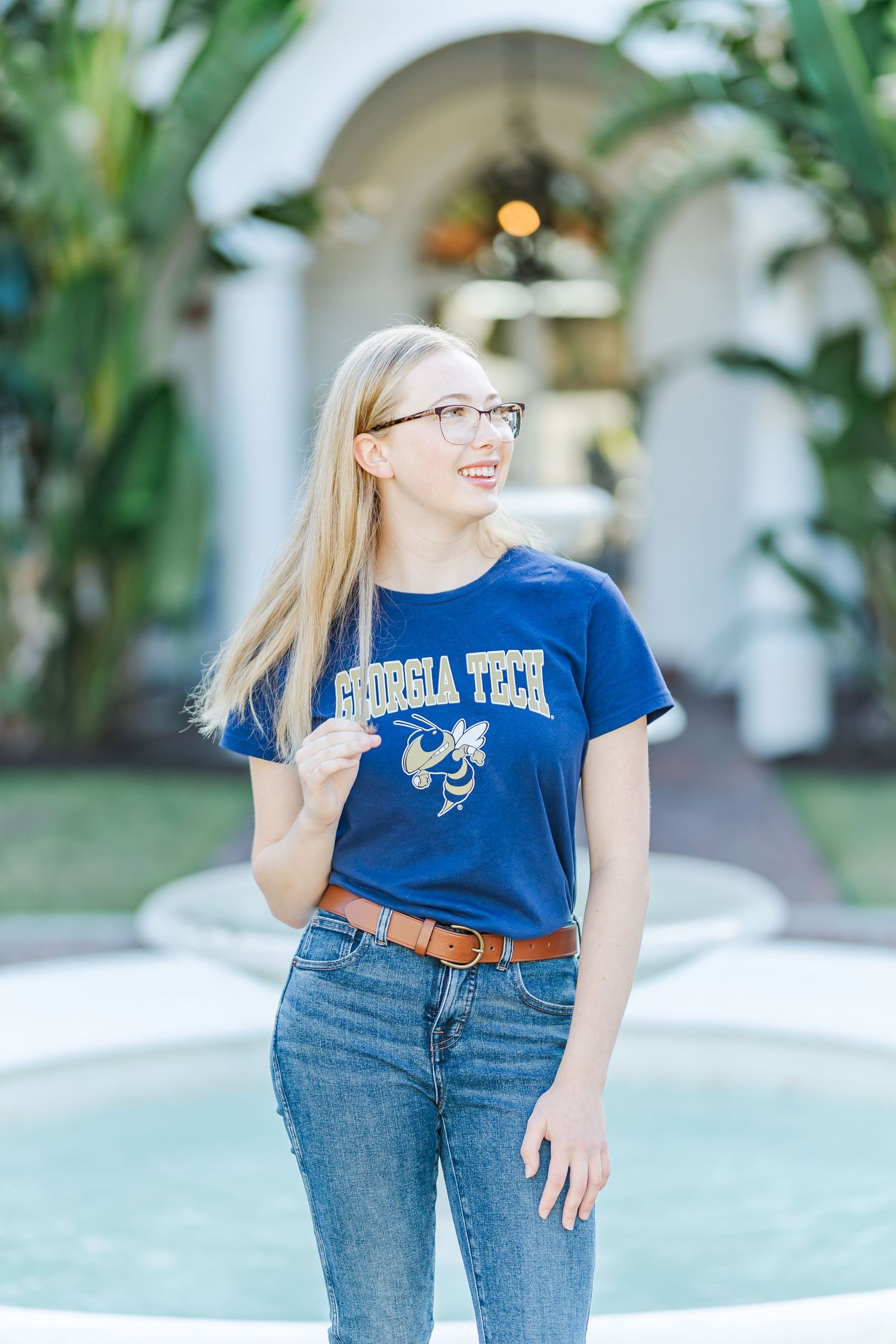 Person in Georgia Tech shirt smiles while standing by outdoor fountain.