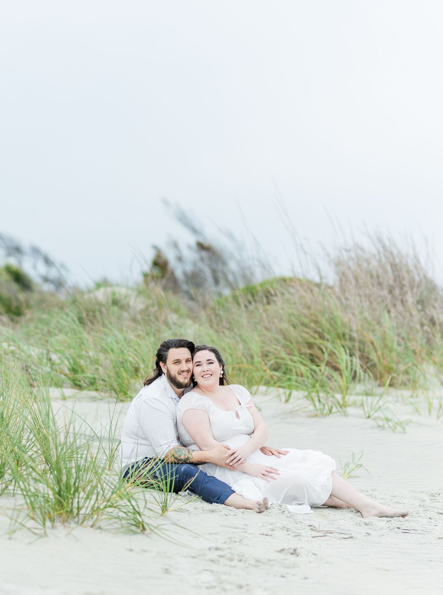 Couple shares intimate moment while sitting together on beach dunes.