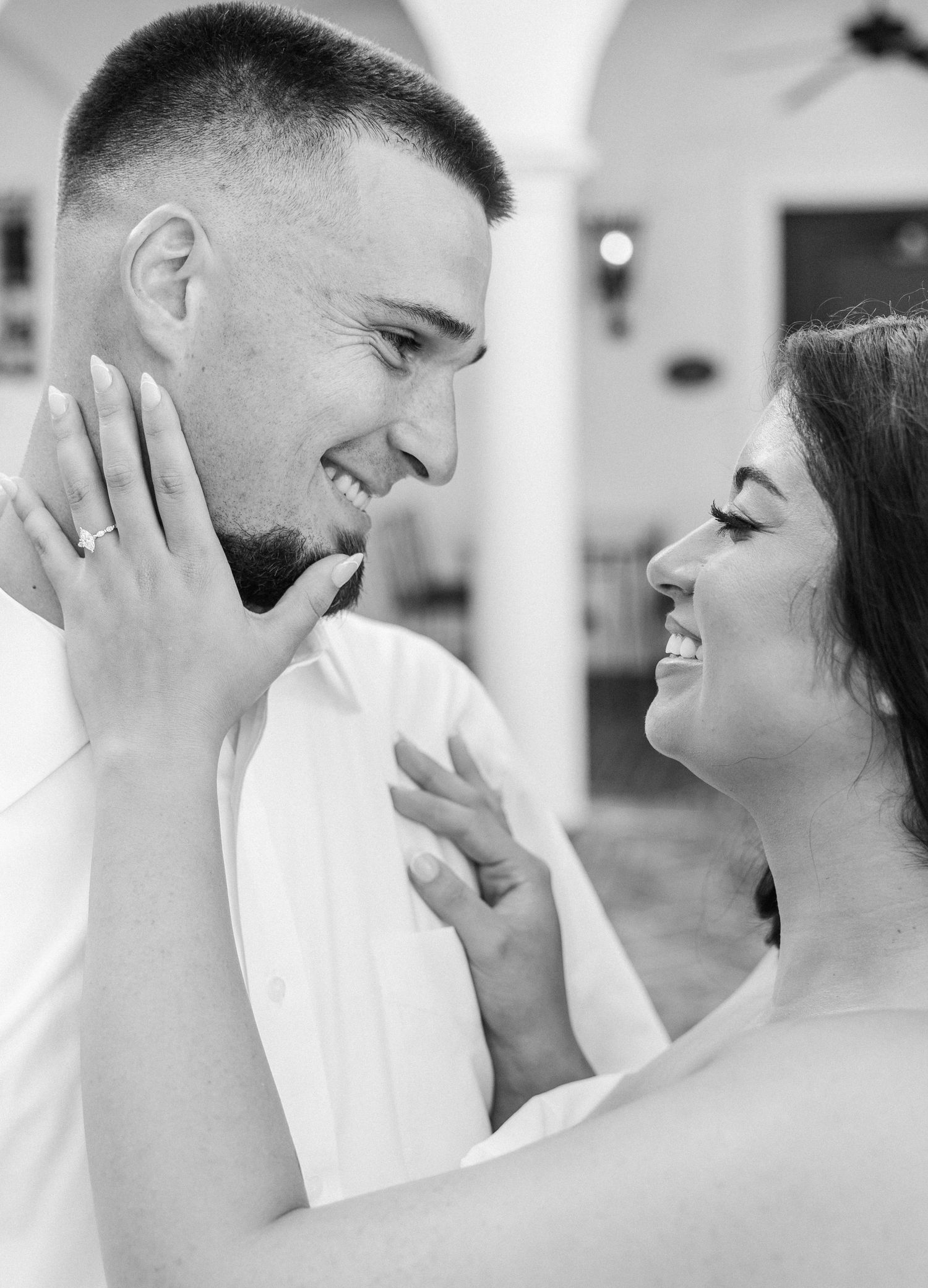 Black and white photo of a smiling couple gazing at each other, woman's hand gently touching man's face.