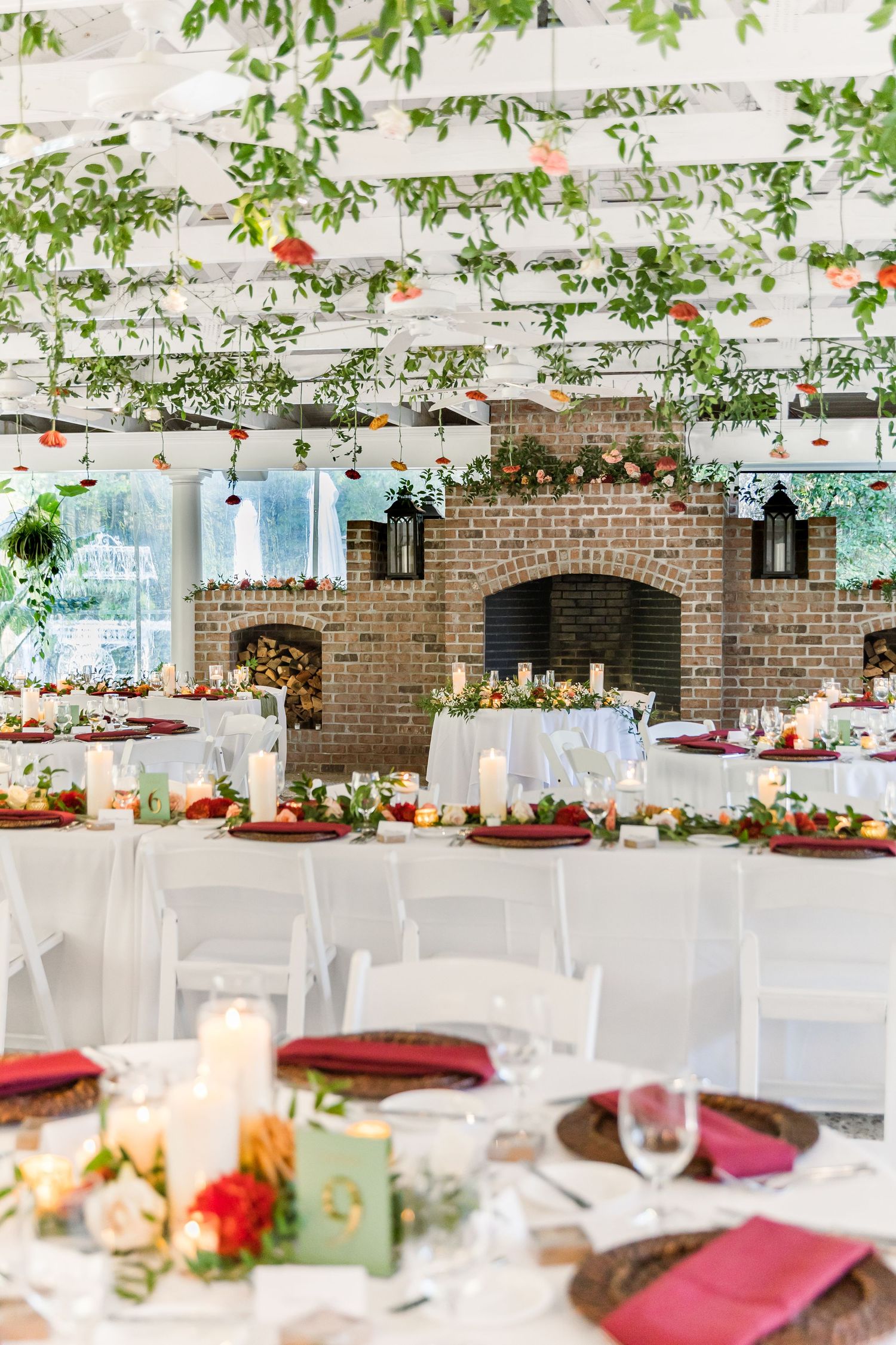 Elegant wedding reception tables with white linens and greenery hanging from above in a rustic brick venue.
