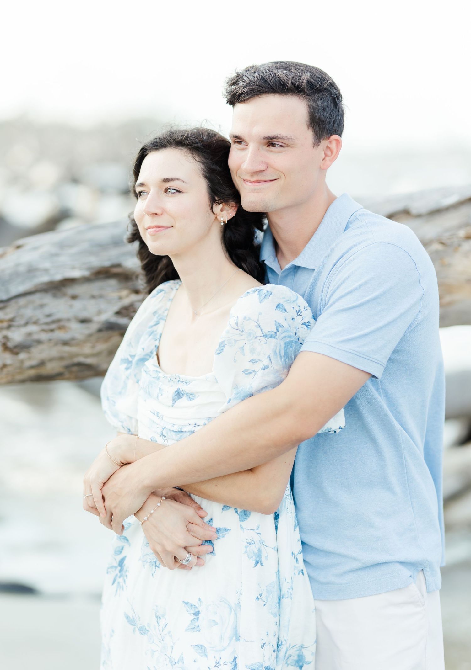 An intimate beachside portrait of a couple embracing in coordinated blue and white outfits.