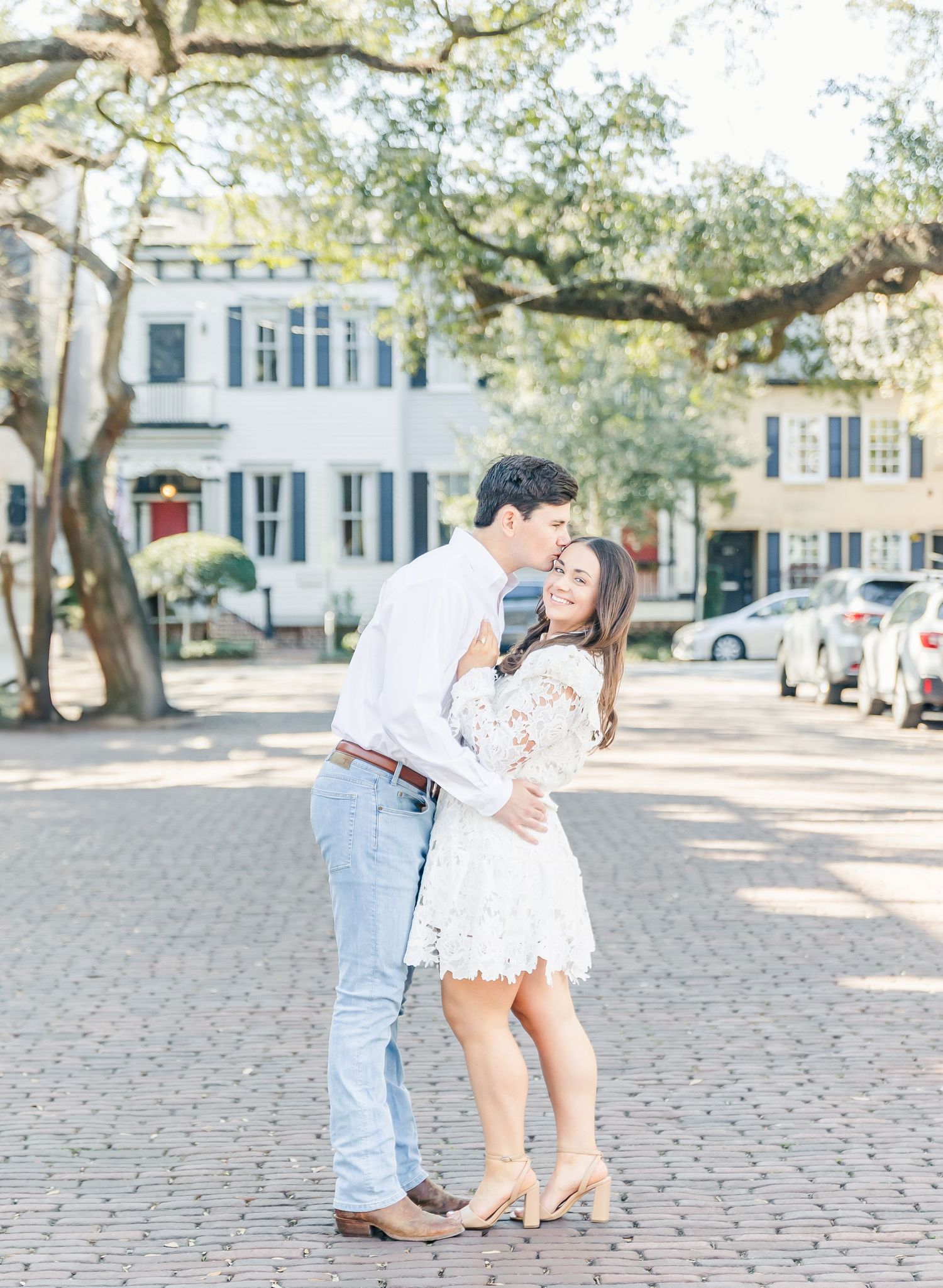 A couple in coordinated light outfits shares an intimate moment on a cobblestone plaza.
