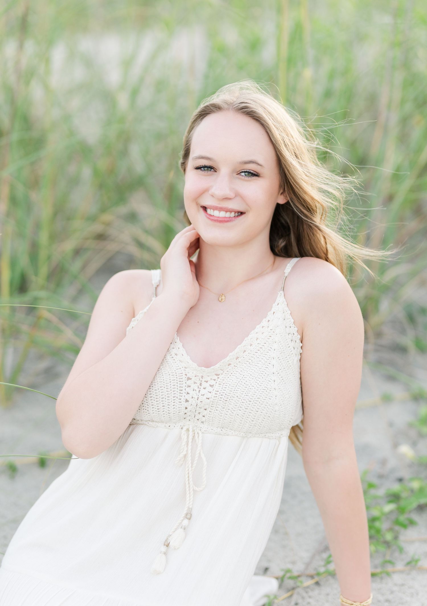 Portrait of someone in a white lace summer dress with windswept hair against a natural beach grass background.