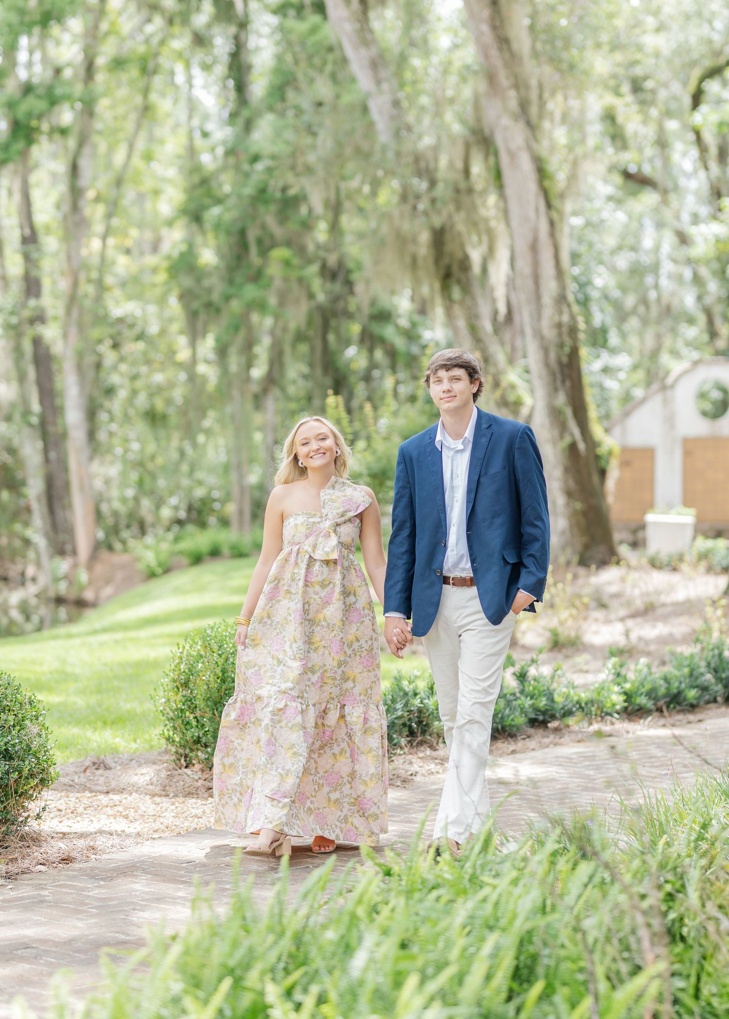 Romantic garden photoshoot featuring couple in coordinated outfits walking among trees.