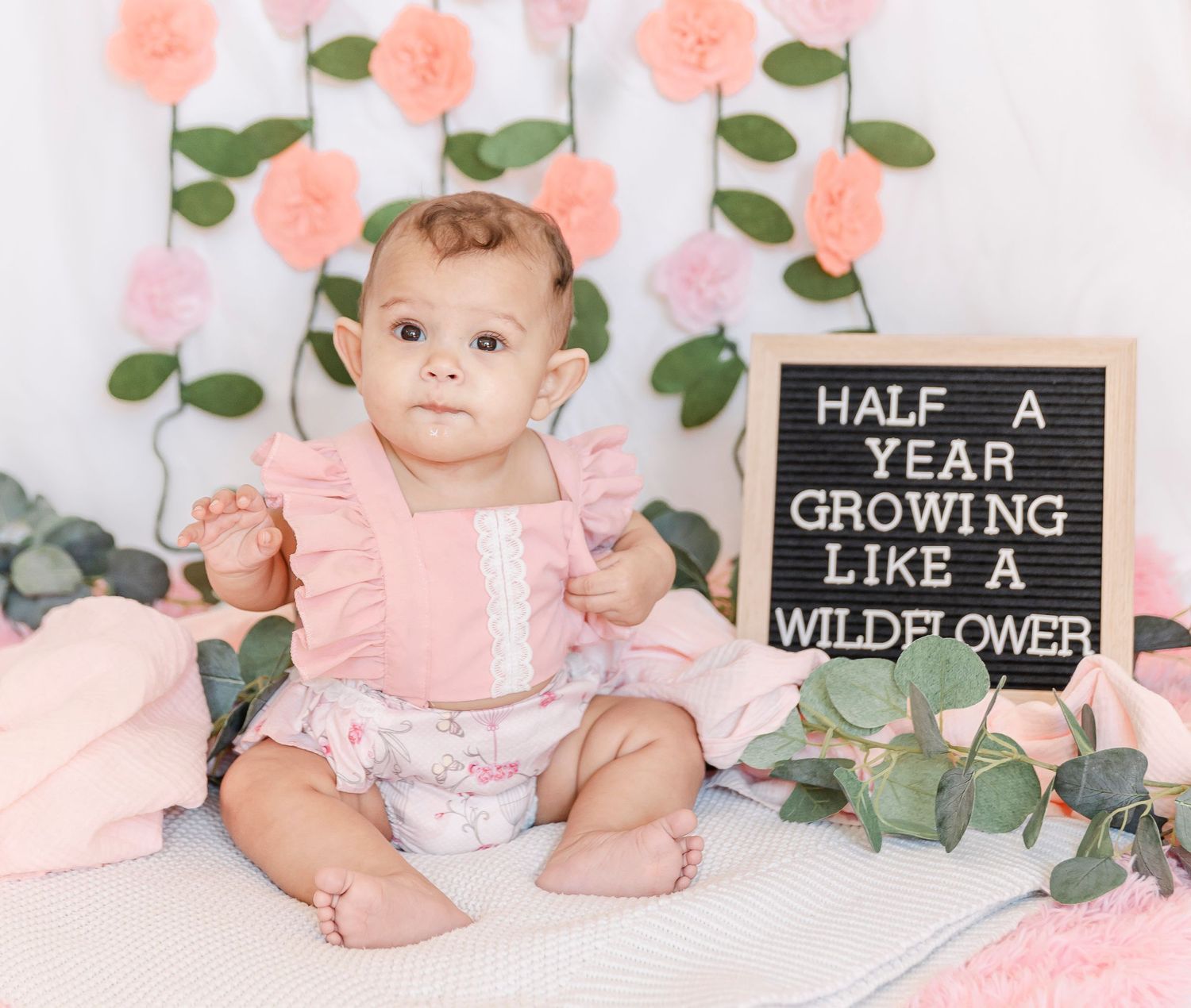 Pink floral themed milestone photoshoot featuring soft decor and a chalkboard sign.