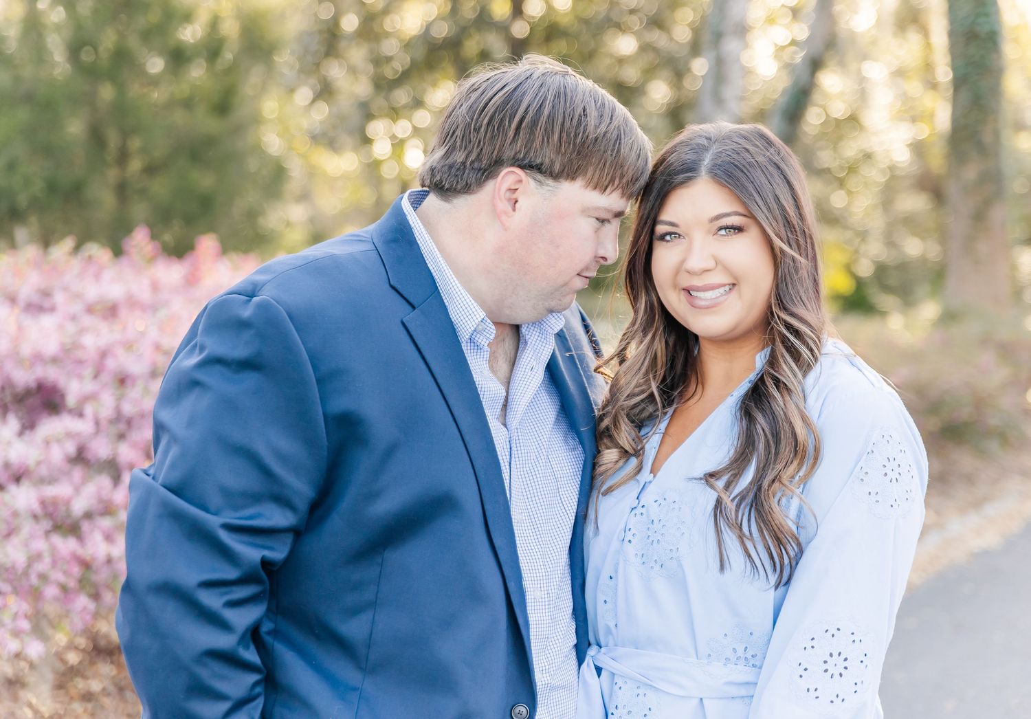 Casual engagement photo of a couple in blue tones with spring blossoms in the background.