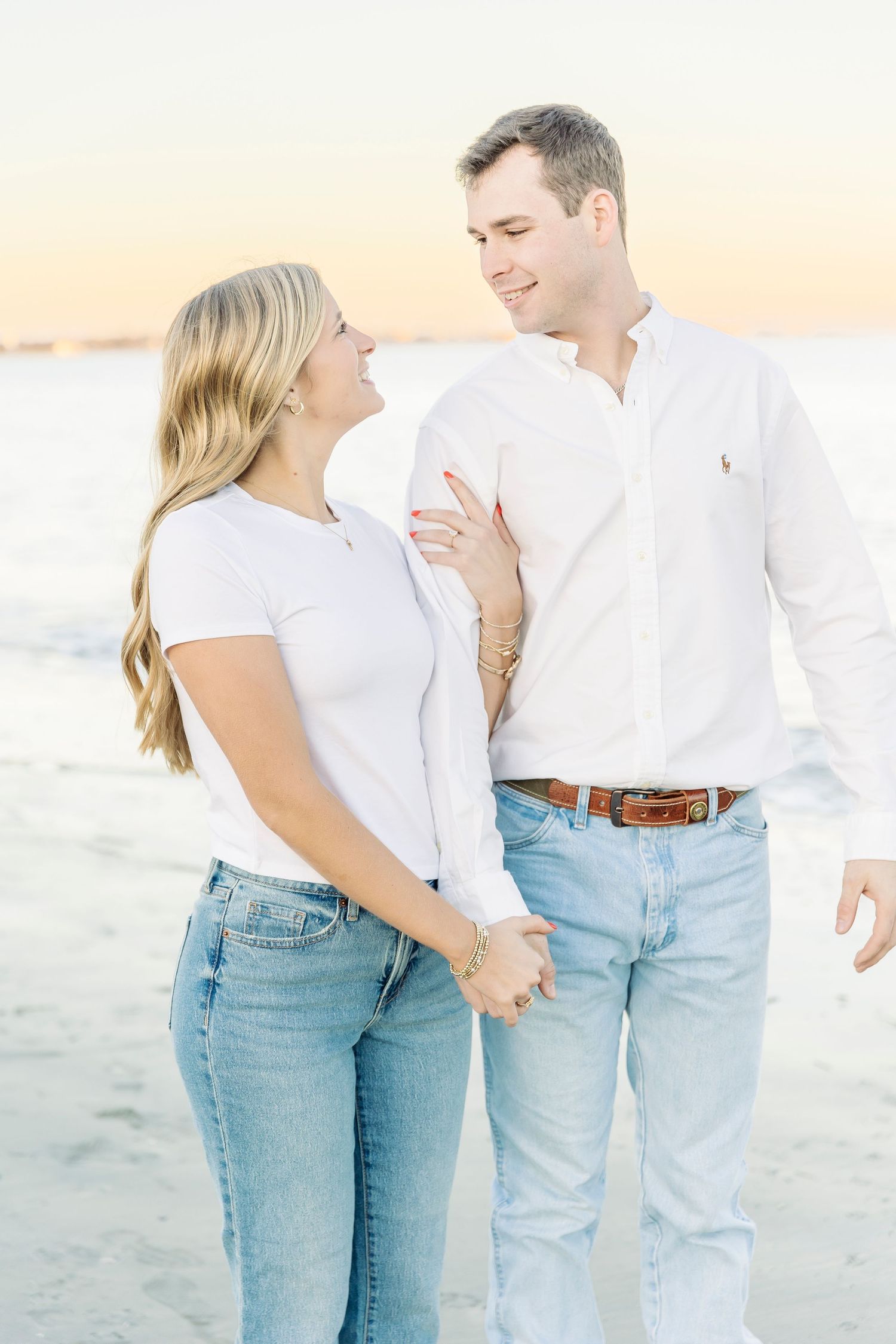 Couple in matching white tops and light denim jeans sharing a romantic moment on the beach.