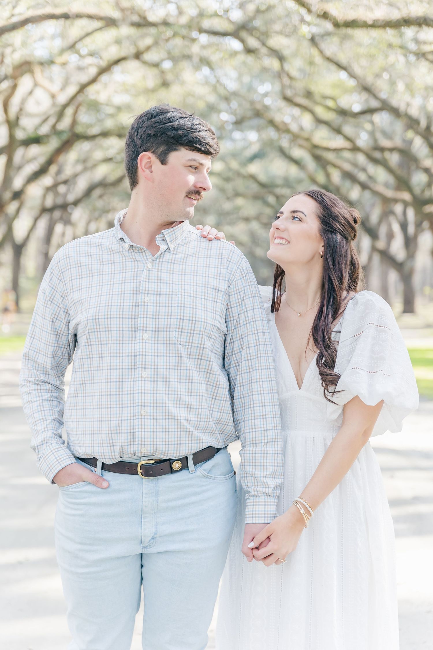 A couple in coordinating outfits shares a loving moment on a tree-lined path.