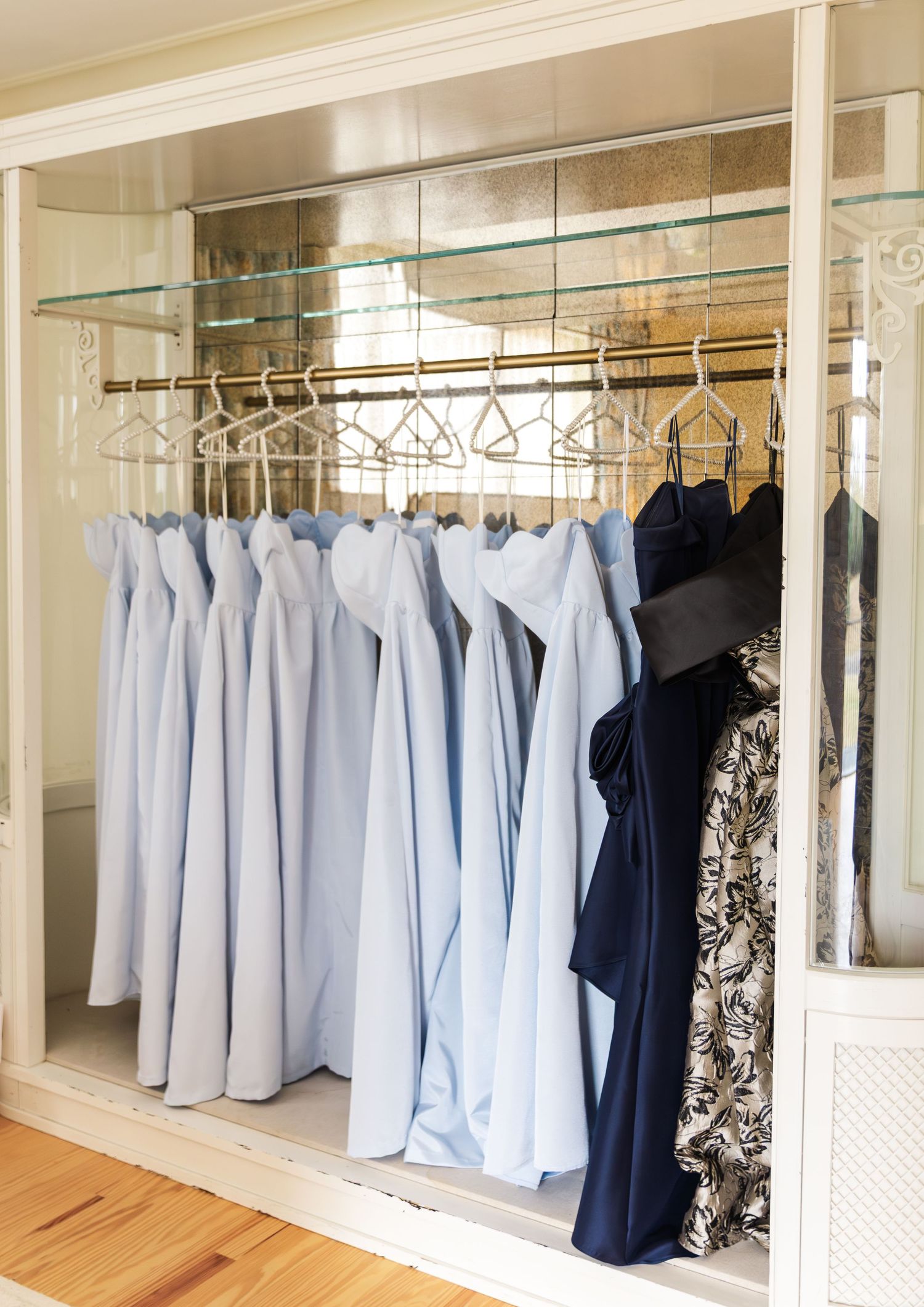 Light blue and navy bridesmaid dresses hanging neatly on gold hangers in a mirrored closet.