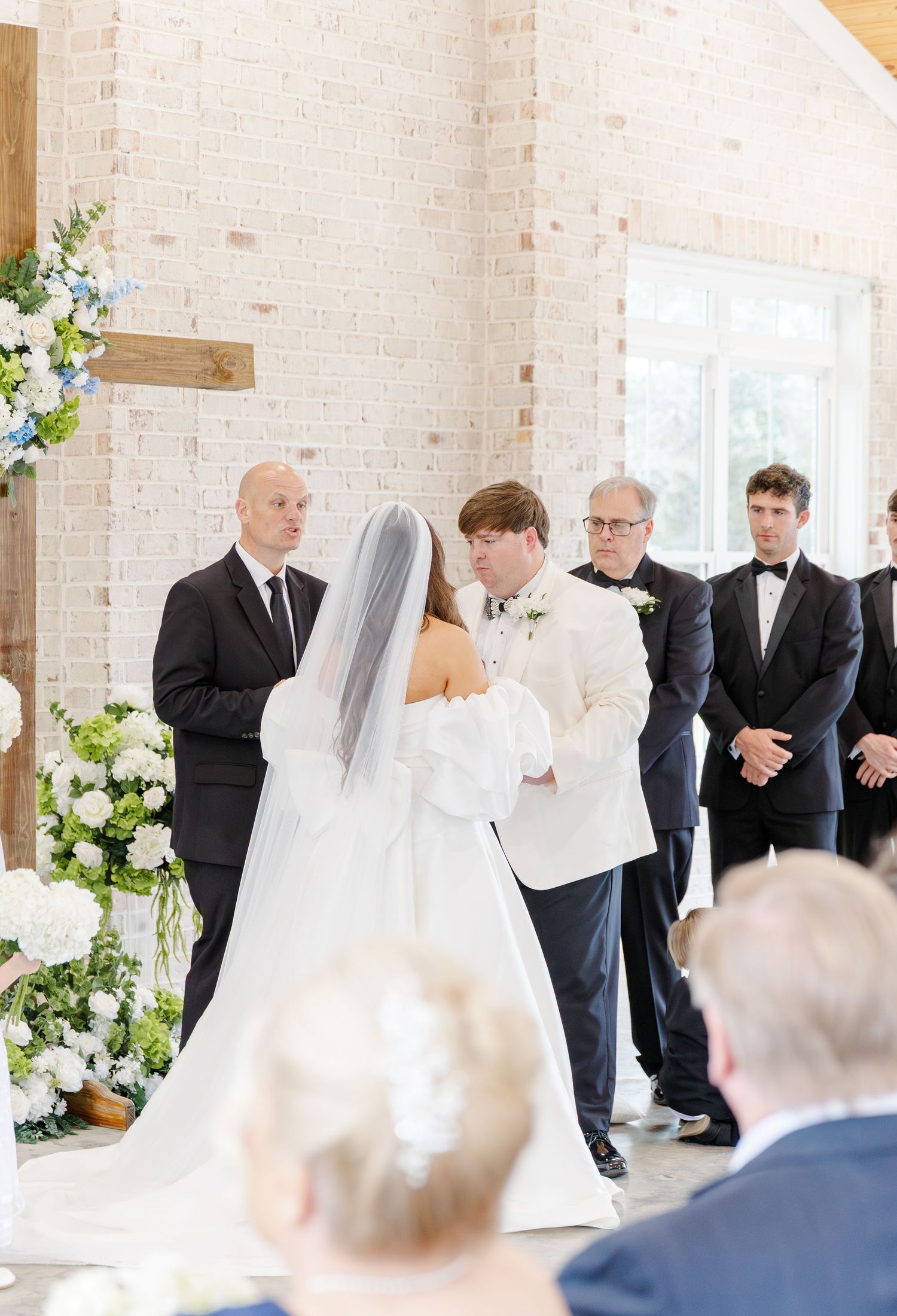 Bride and groom exchanging vows at altar decorated with white and blue floral arrangements in chapel.