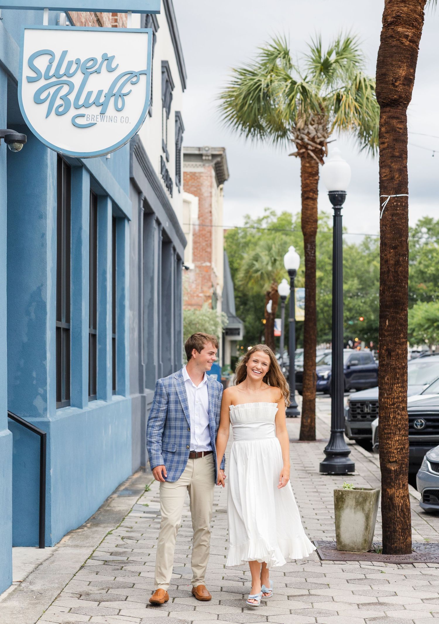Couple walking and smiling outside Silver Bluff Cafe on a charming downtown sidewalk lined with palm trees.