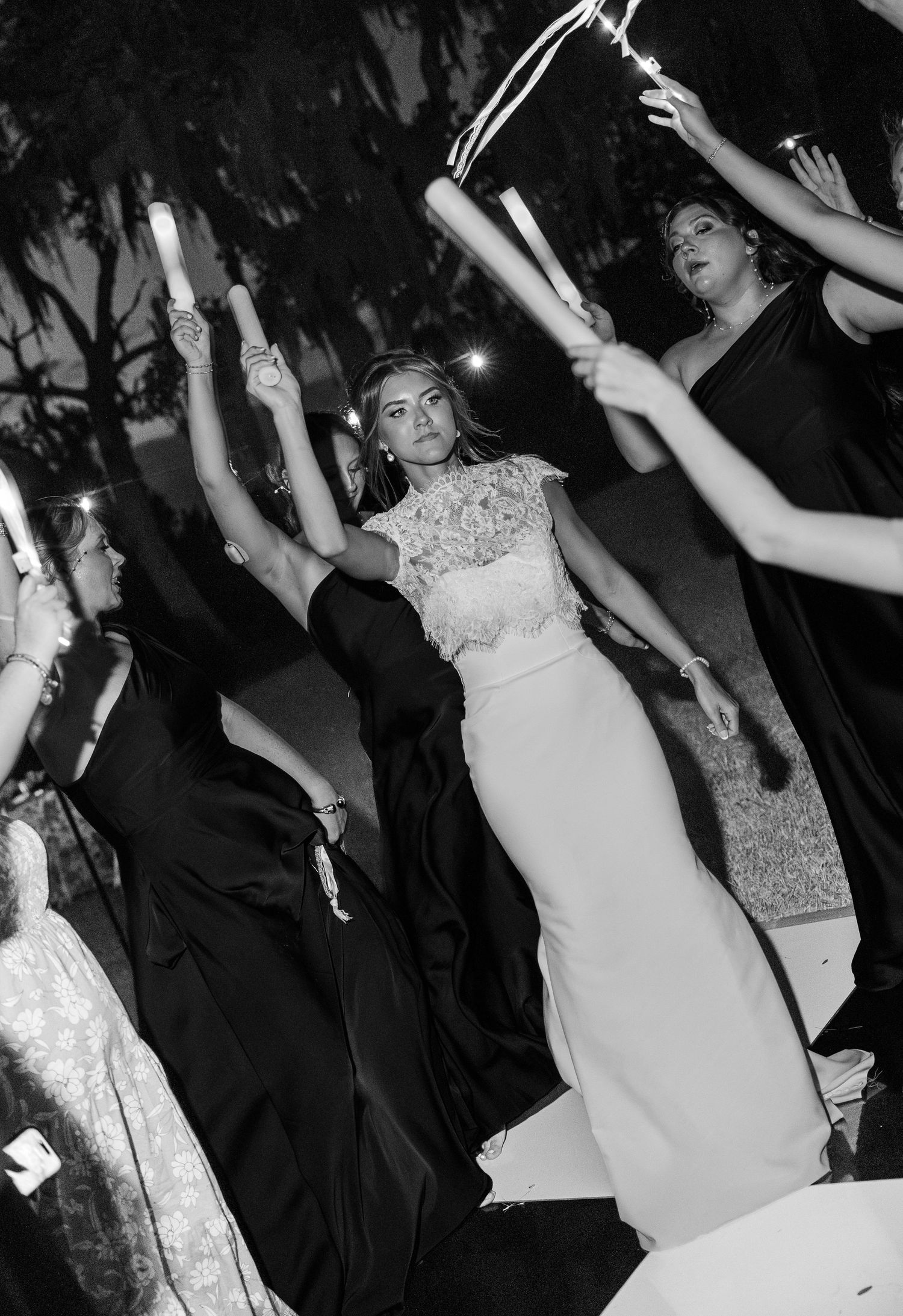 Bride in white lace gown surrounded by bridesmaids holding candles at night wedding celebration.