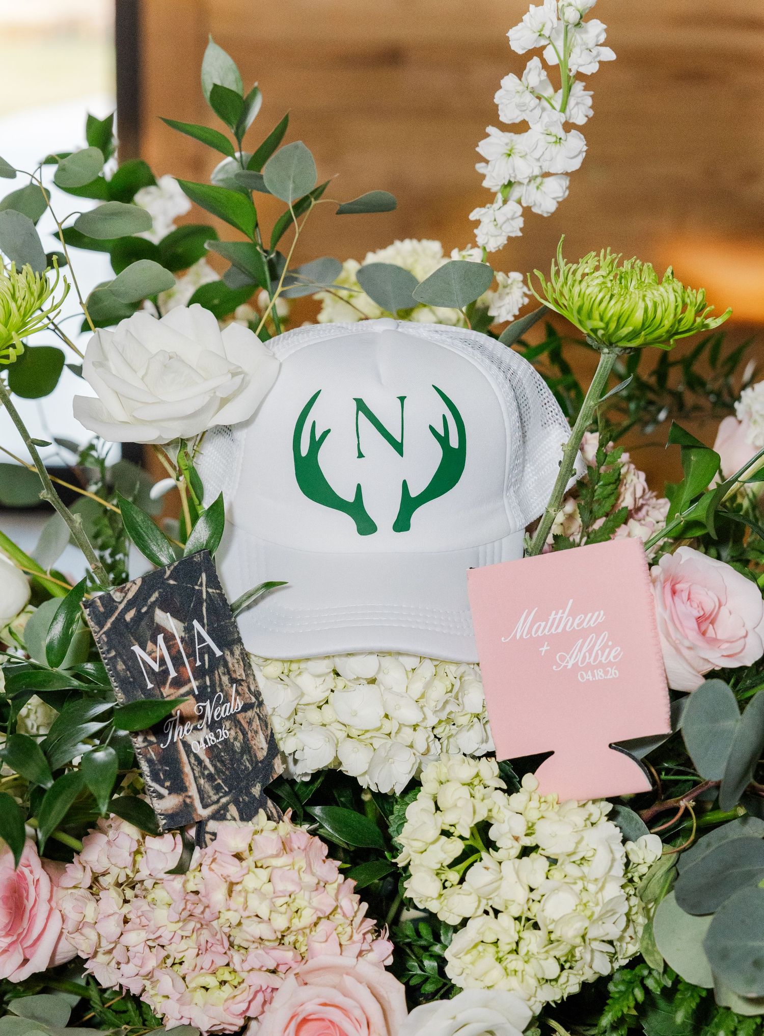 Wedding decor display with white cap, antler monogram N, pink koozies, and floral arrangement.