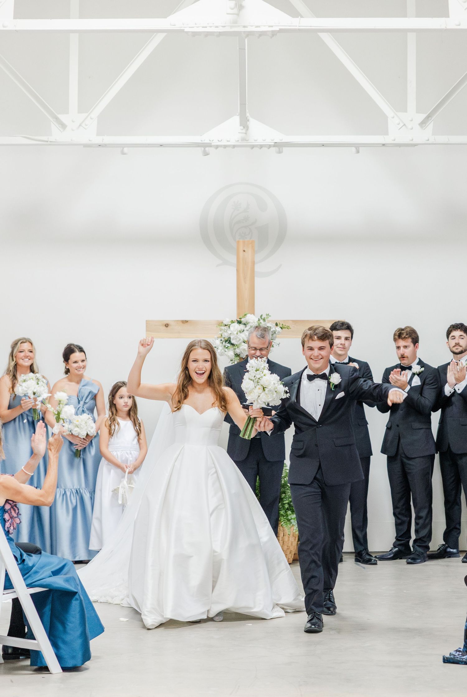 Newlyweds celebrate joyfully at altar with bridesmaids in blue and groomsmen in black tuxedos.