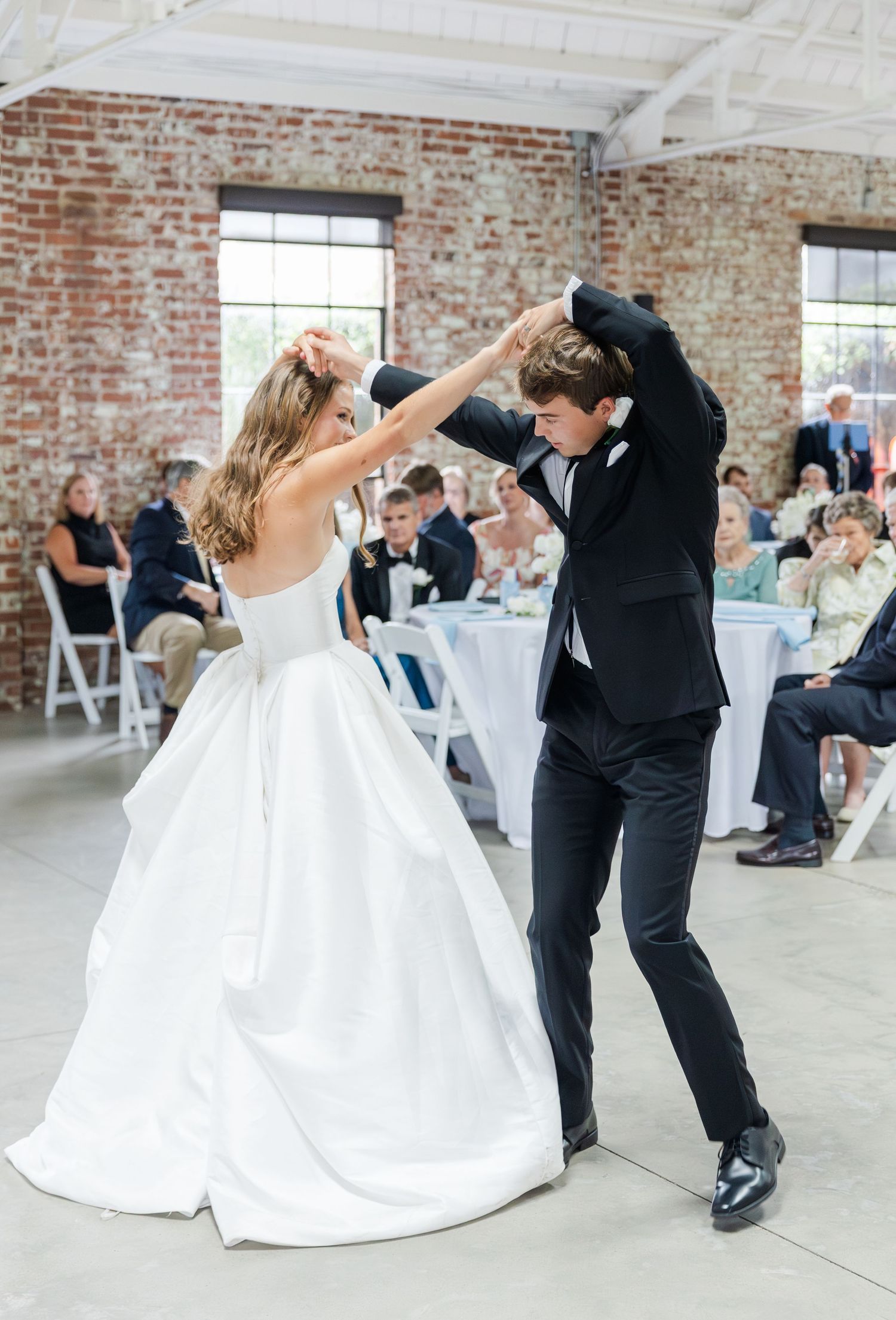 Bride and groom share first dance spin in white ball gown at rustic brick wedding reception.