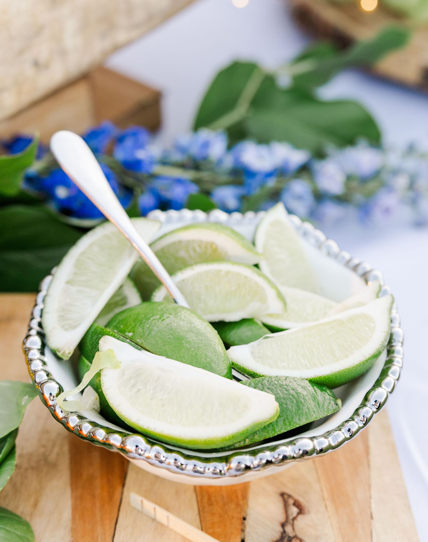 Fresh lime wedges arranged in a silver beaded bowl with a spoon for wedding cocktail garnishes.