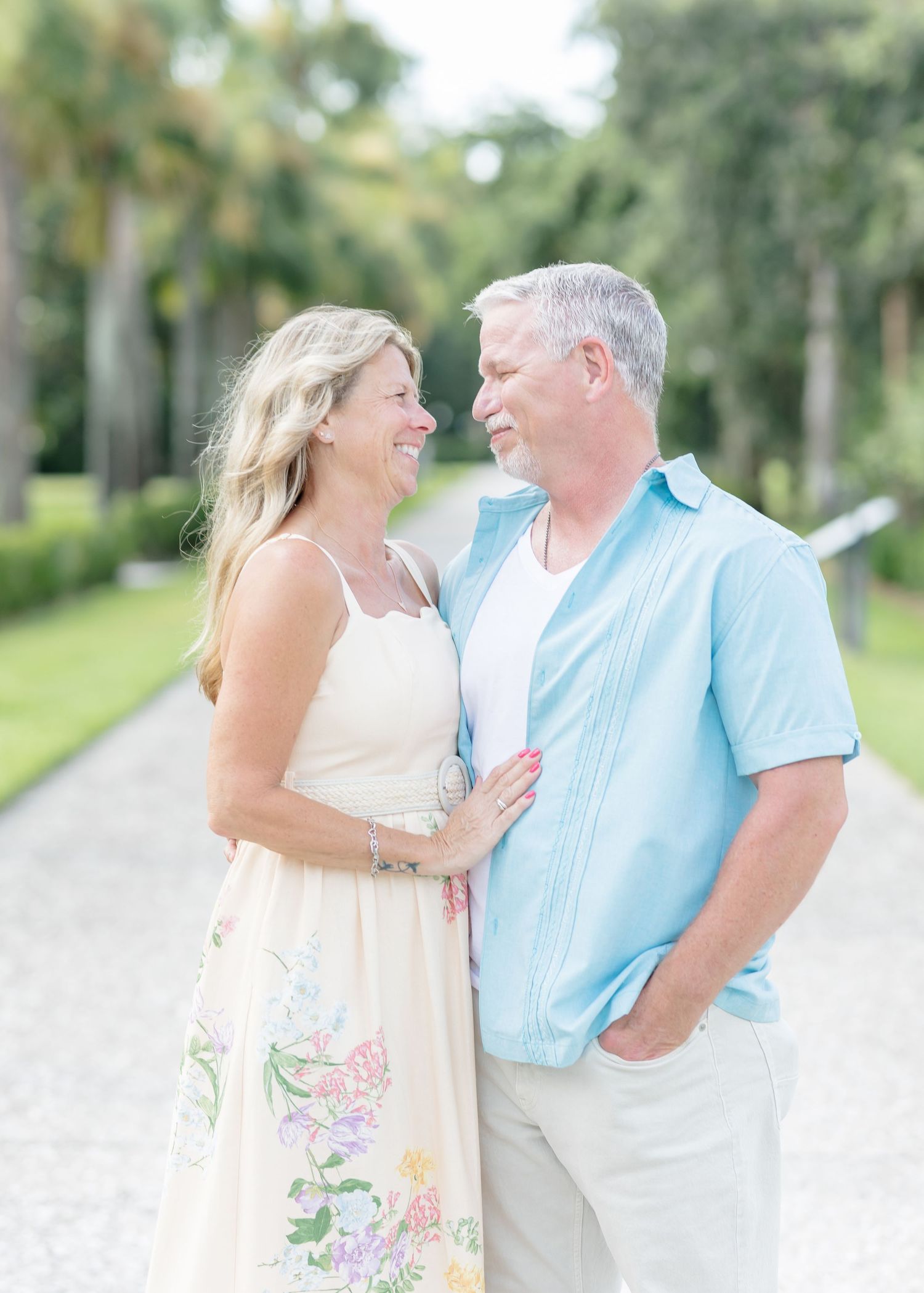 A couple shares a loving moment outdoors in a garden setting, wearing light summer clothing in pastel colors.