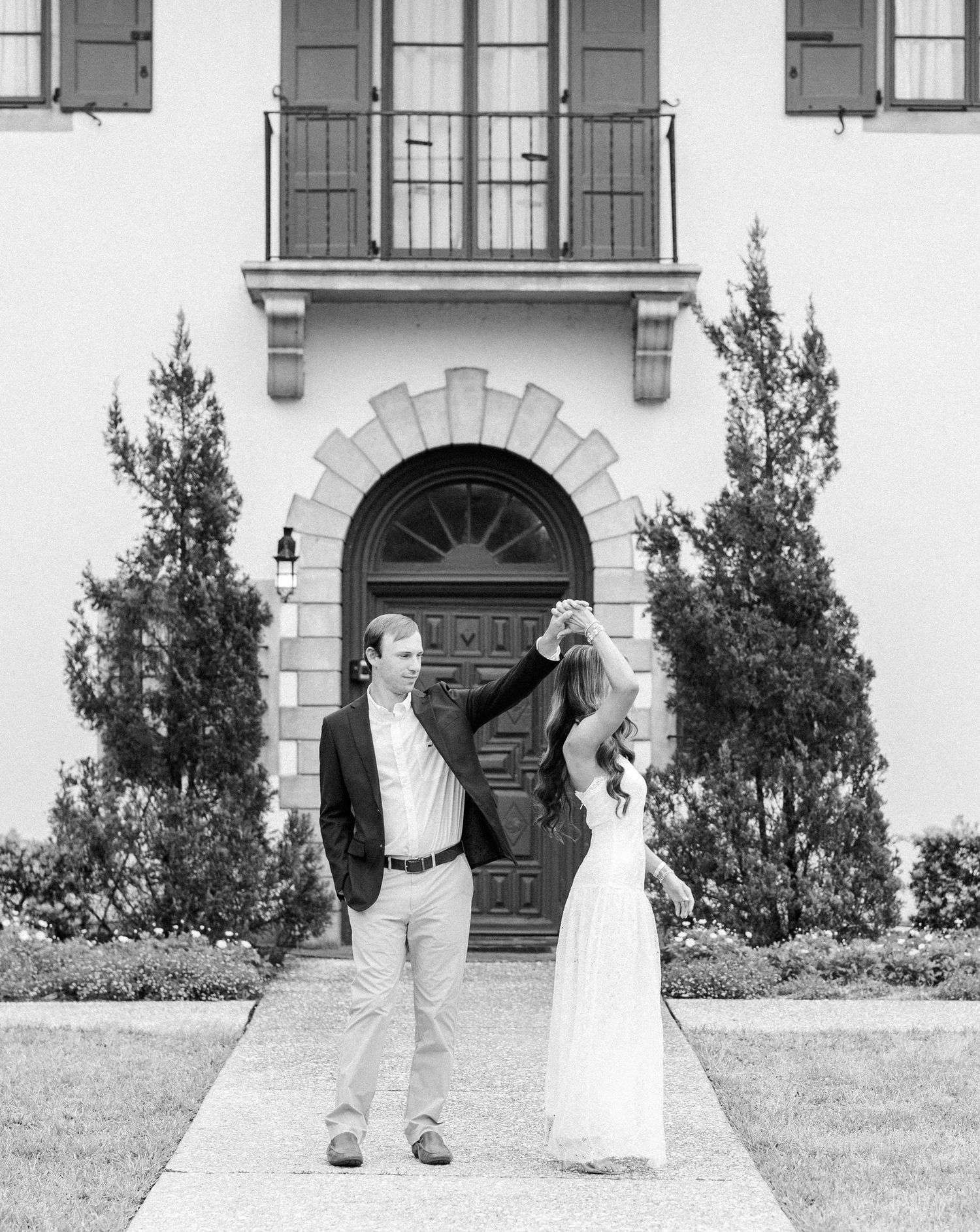 Black and white photo of couple dancing in front of elegant white building with arched doorway.