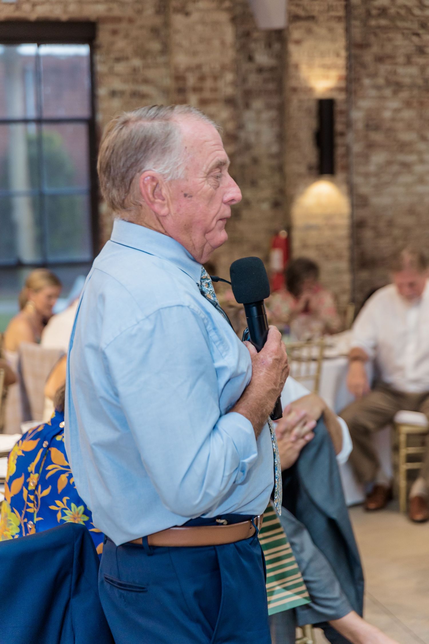 Speaker delivering a heartfelt speech during wedding reception in brick-walled venue.