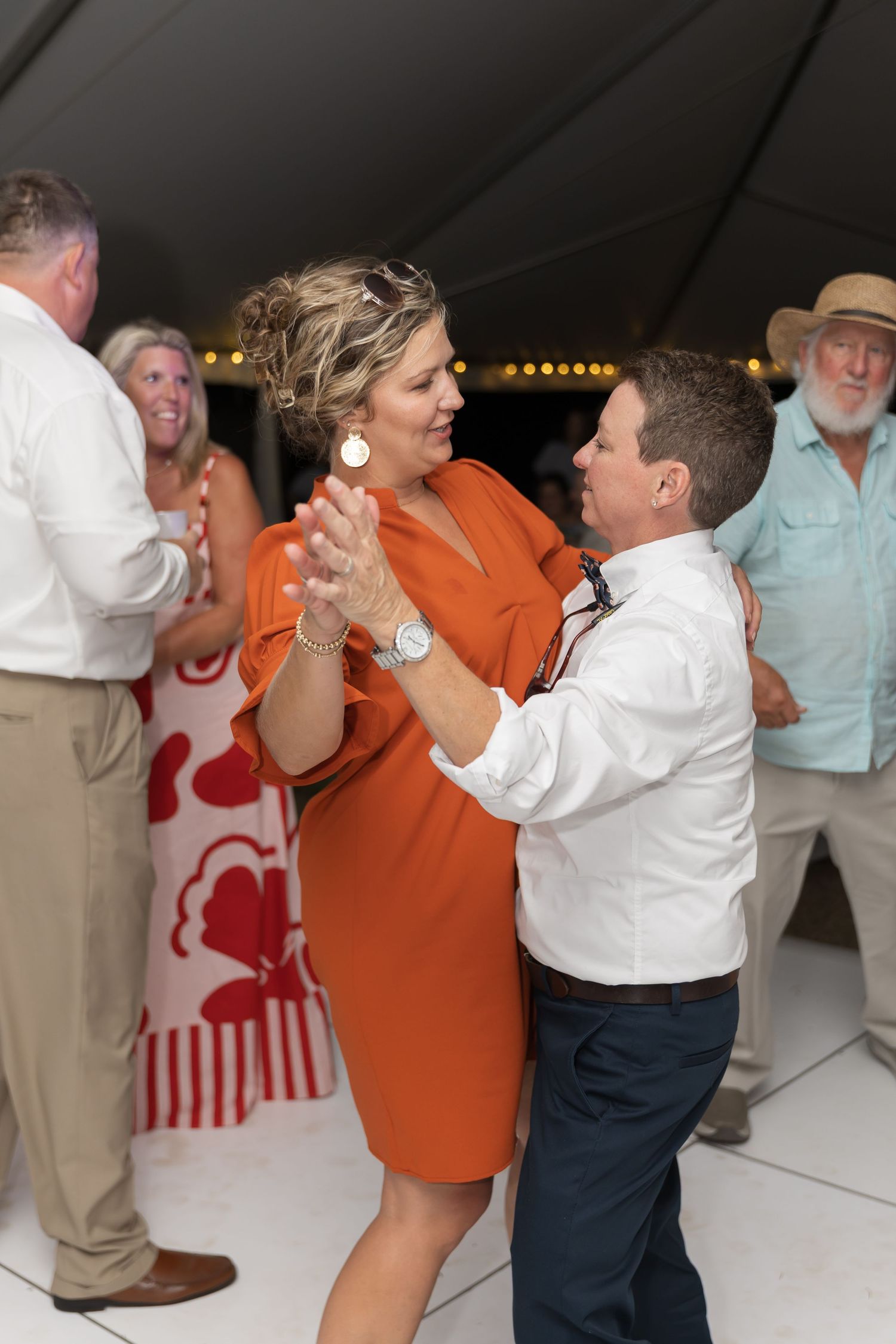 Wedding guests dancing and celebrating at a reception under a tent with string lights.