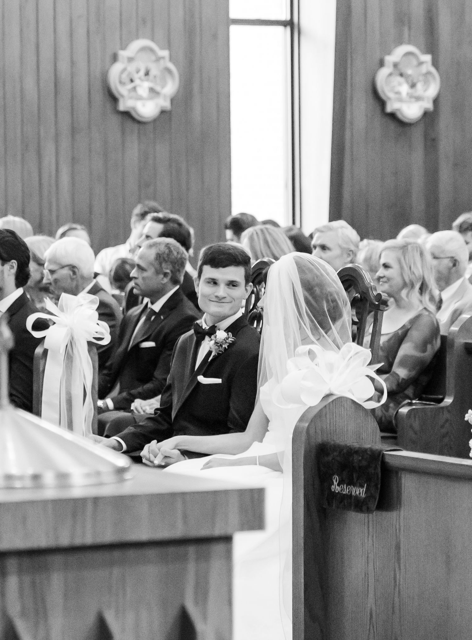 Black and white photo of wedding guests seated in church pews during a ceremony.