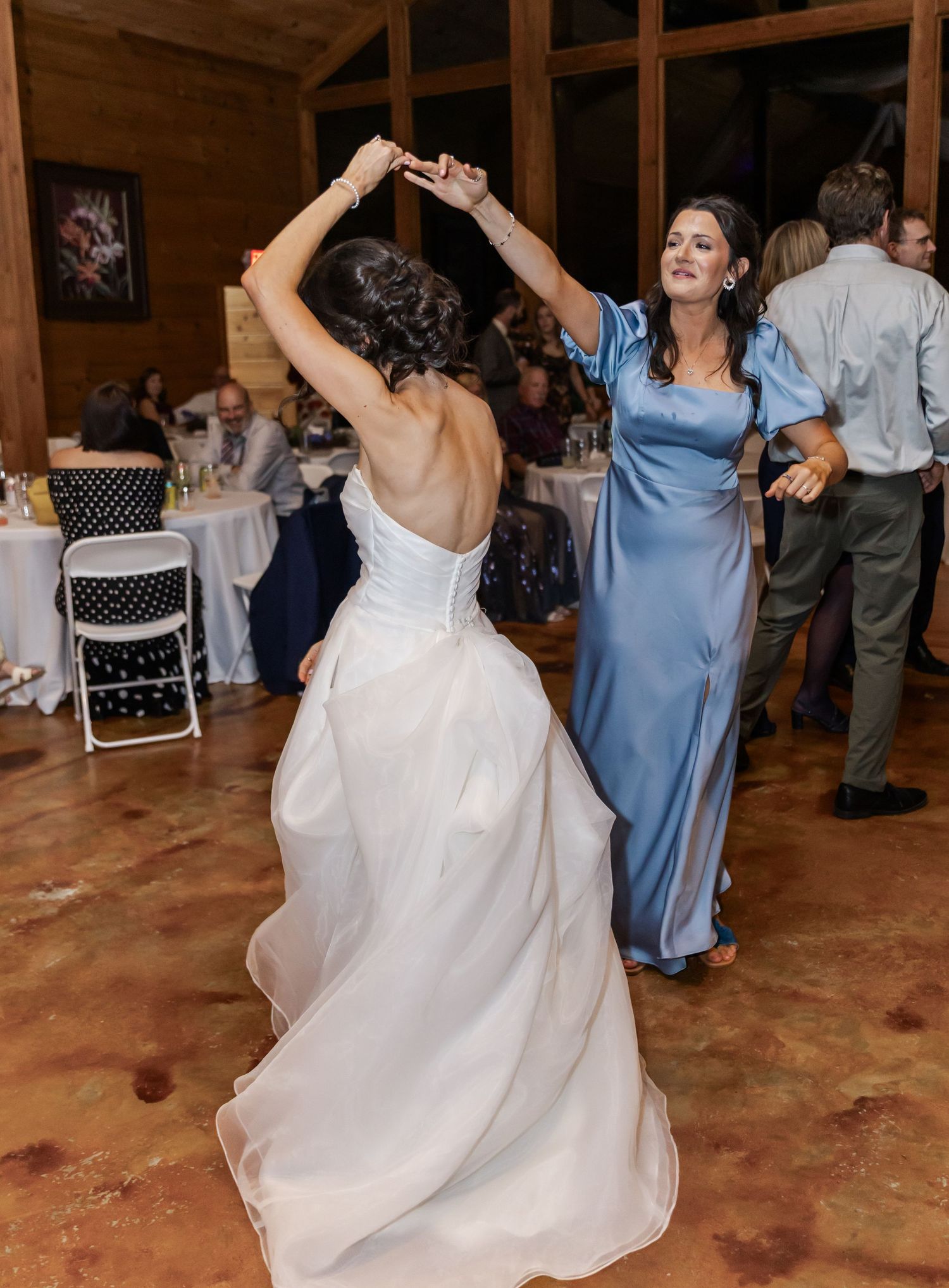 Wedding guests and the bride dance joyfully at a rustic barn reception venue.