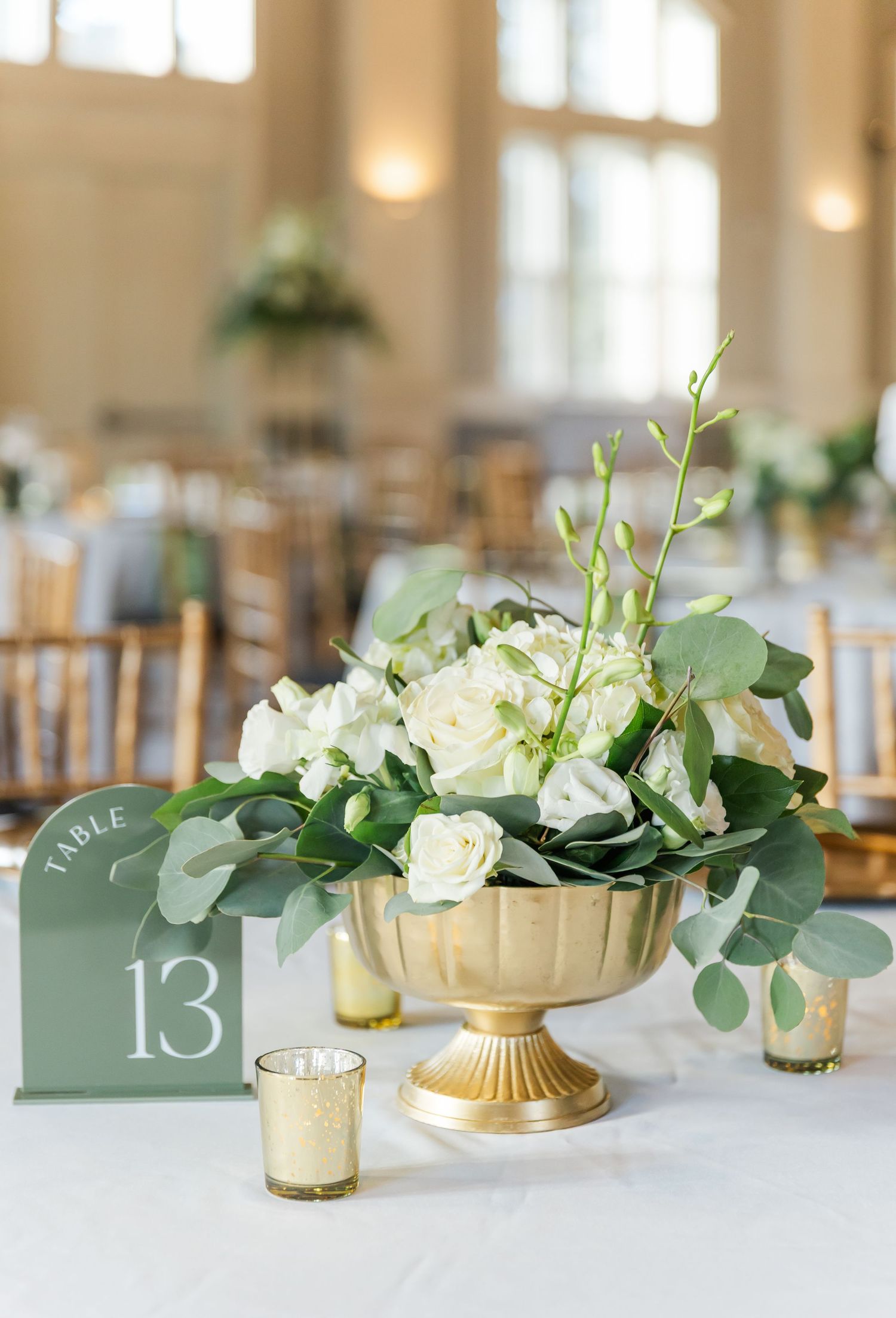 Elegant wedding reception table with gold vases, white roses, eucalyptus greenery and sage green table numbers.
