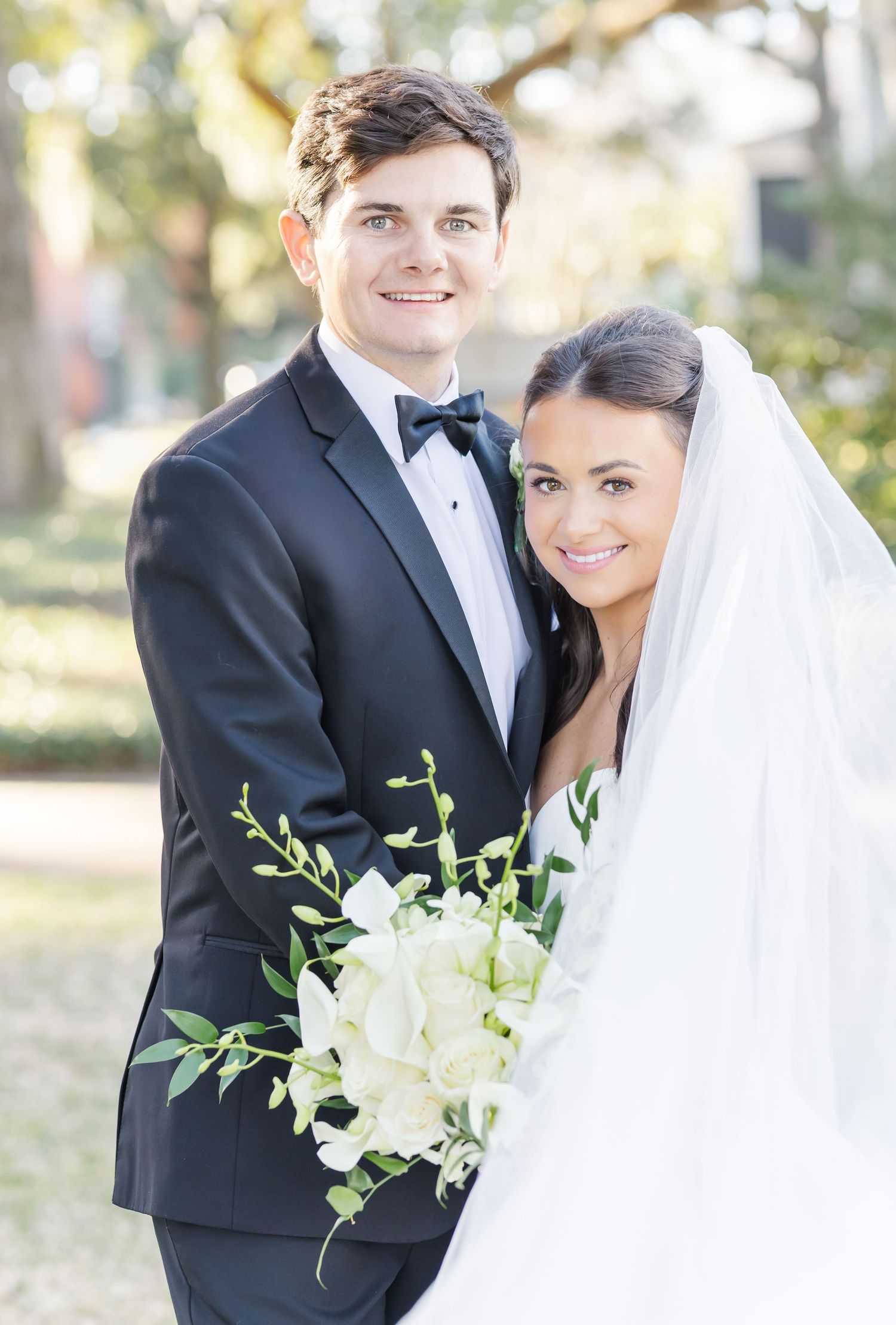 Elegant outdoor wedding portrait with white floral bouquet and formal attire.
